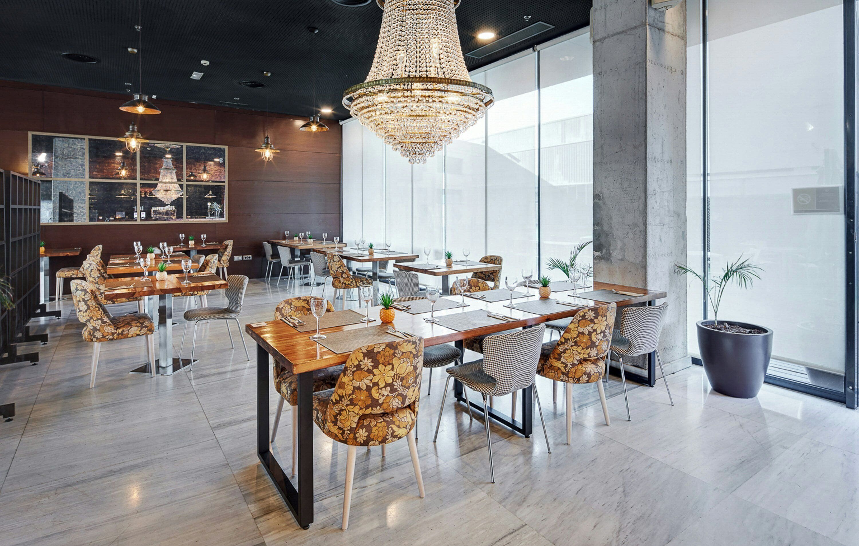 Un restaurante moderno con candelabro, mesas de madera y sillas estampadas.
