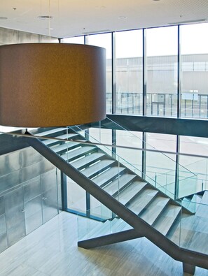 Ein modernes Interieur mit einer Glaswendeltreppe, einer großen zylindrischen Leuchte und Blick durch große Fenster.