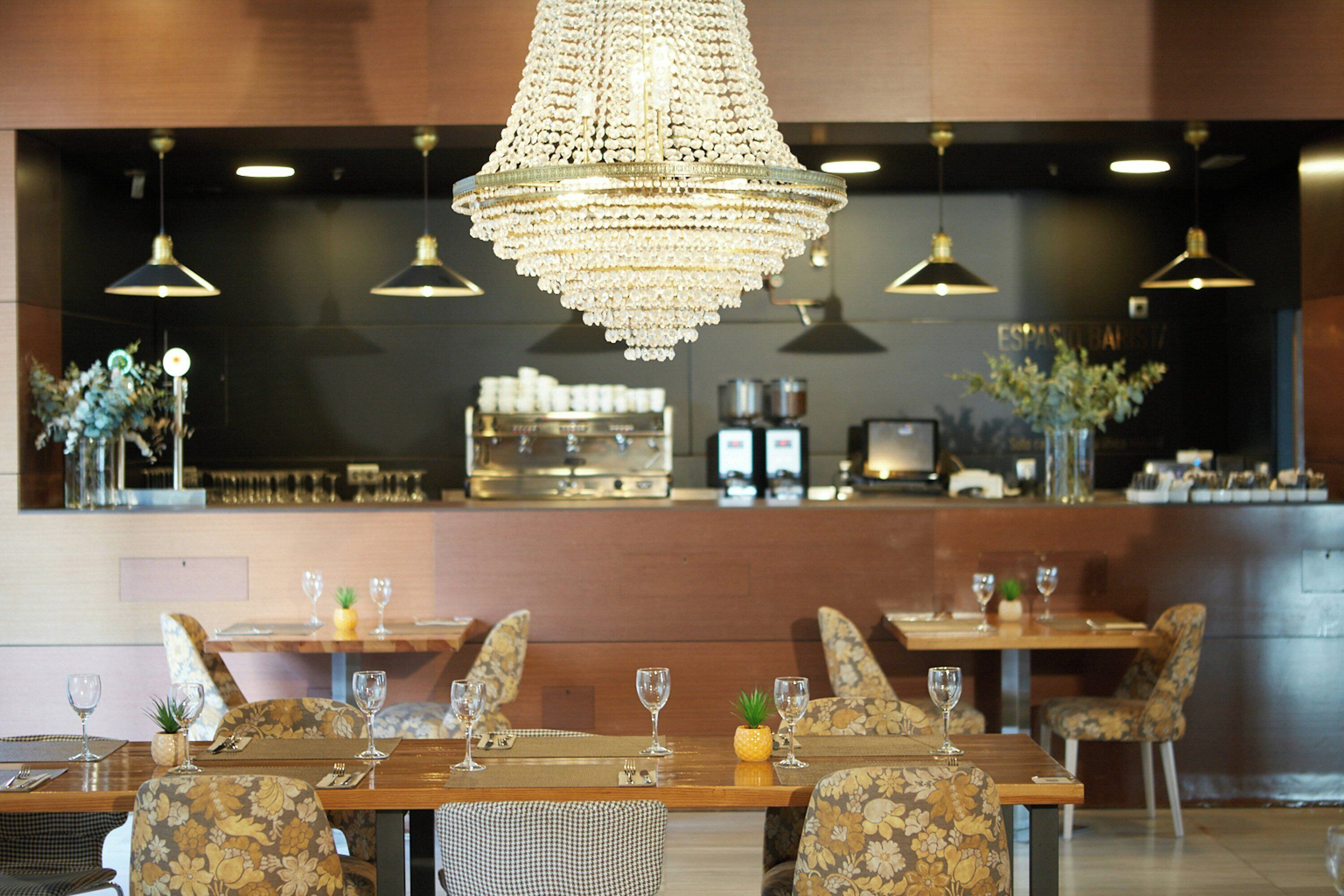 Interior de un restaurante con barra, mesas dispuestas con copas de vino y un candelabro.