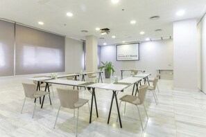 Ein Konferenzraum mit einer großen Leinwand, weißen Tischen und Stühlen mit Zickzackmuster.