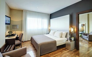 Ein Hotelzimmer mit einem Bett, Nachttischen, einem Schreibtisch, einem Sessel, einem Fernseher und einem großen Spiegel.