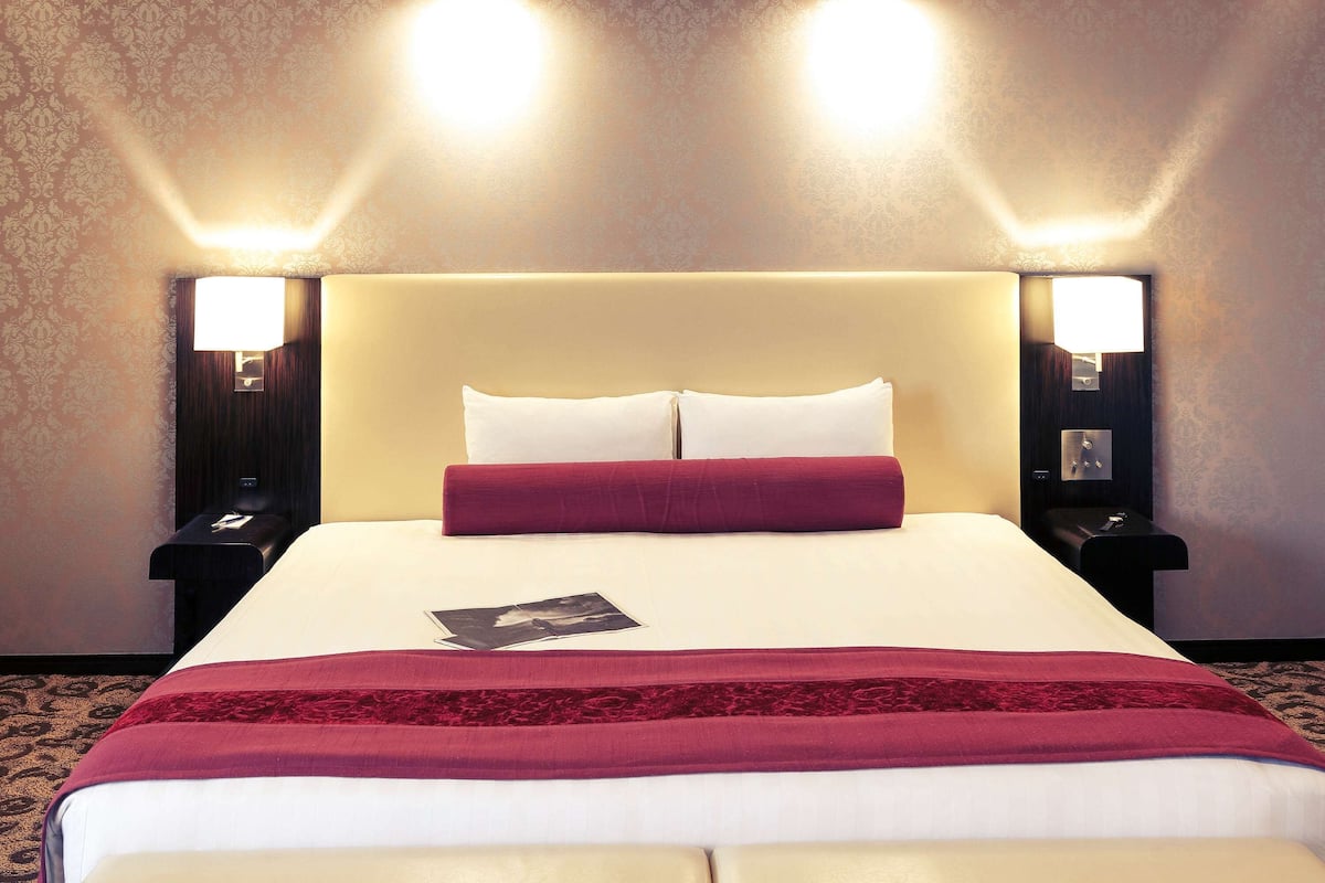 A hotel room with a large bed, two bedside lamps, and a nightstand.