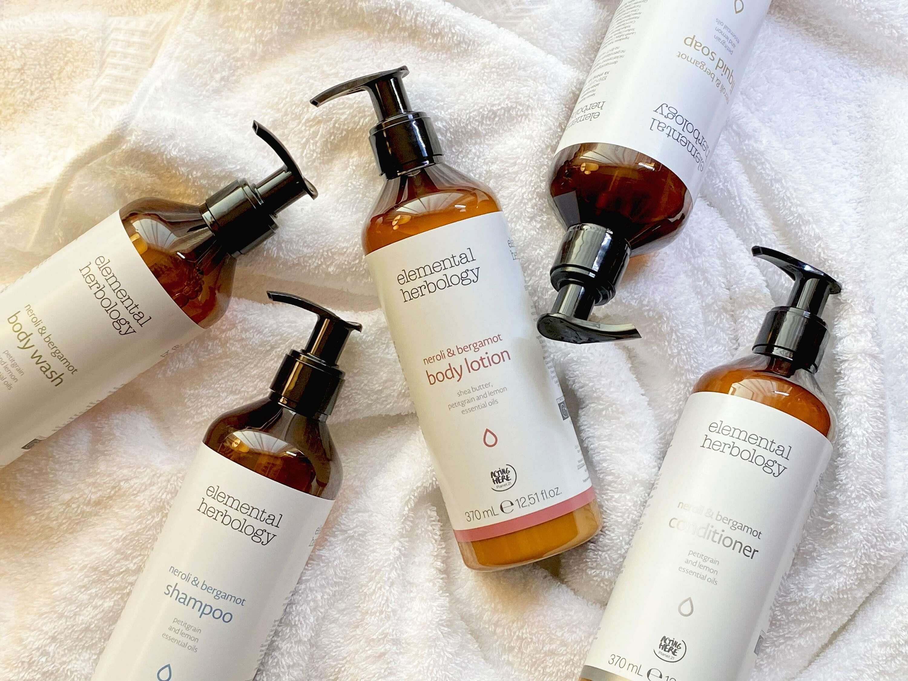 Cuatro botellas de jabón corporal y acondicionador Elemental Herbology sobre una toalla blanca.