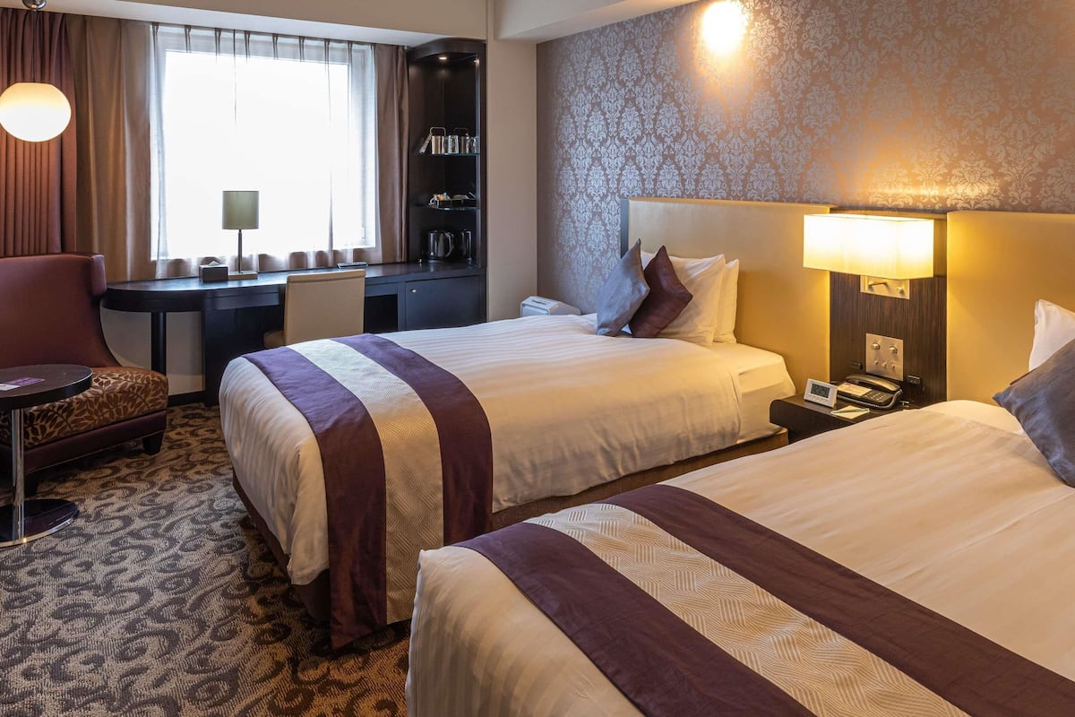 A hotel room with two beds, a desk, a chair, and a window with curtains.