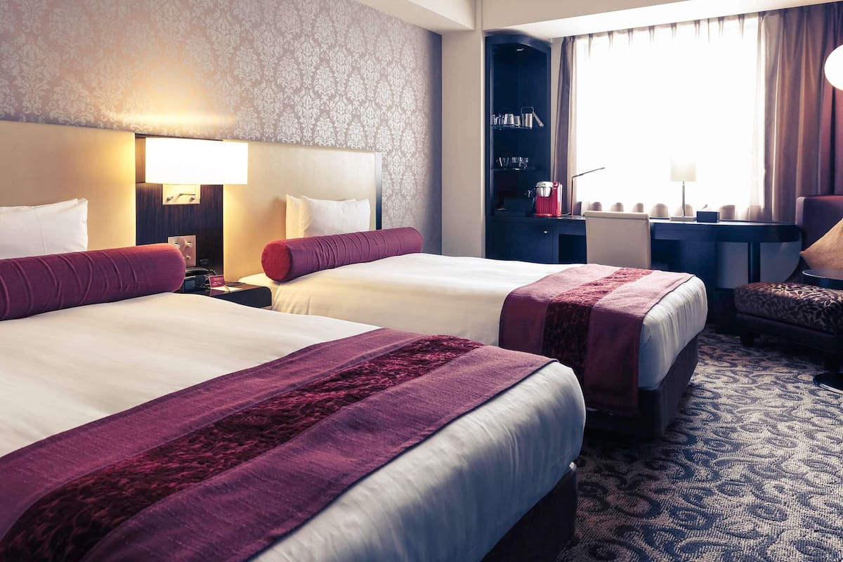 A hotel room with two beds, a desk, a chair, and a wardrobe.