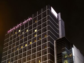 Un hotel alt amb una estructura de finestres quadrades i un cridaner cartell de neó que diu "Mercure Hotel".