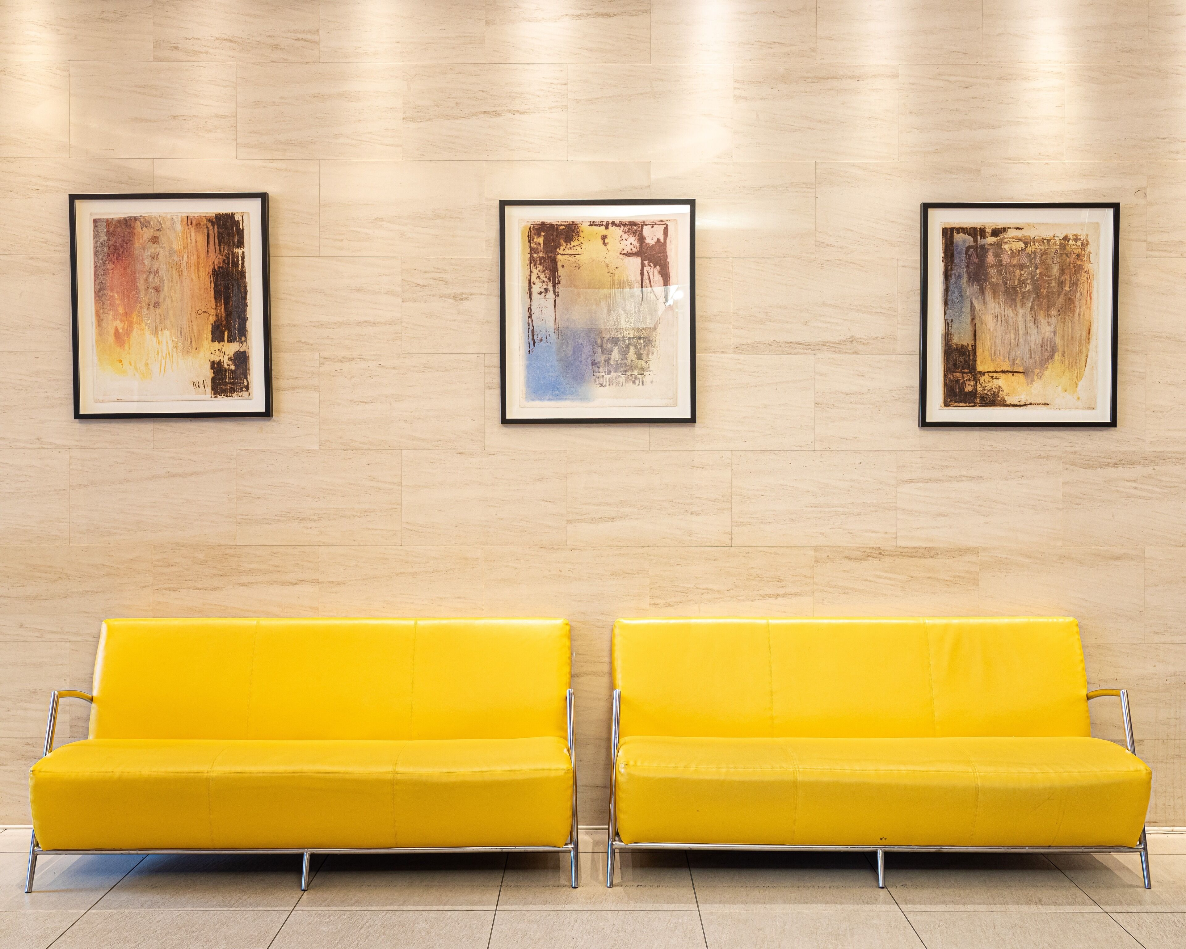 A modern lobby with two yellow sofas and three abstract paintings on the wall.