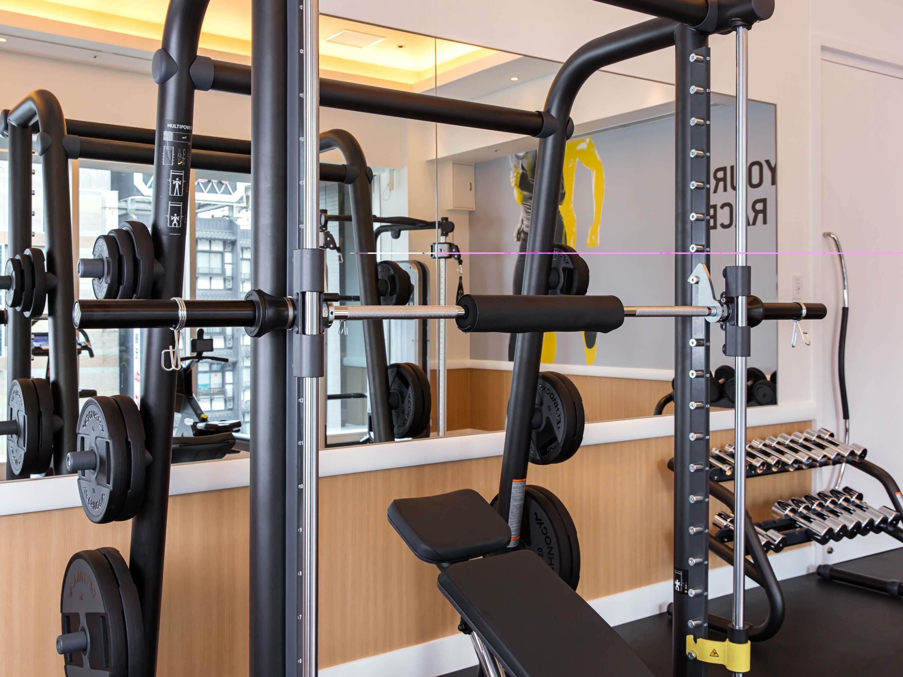 A gym with weightlifting equipment, a bench, and a mirror reflecting the interior.