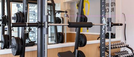 A gym with weightlifting equipment, a bench, and a mirror reflecting the interior.
