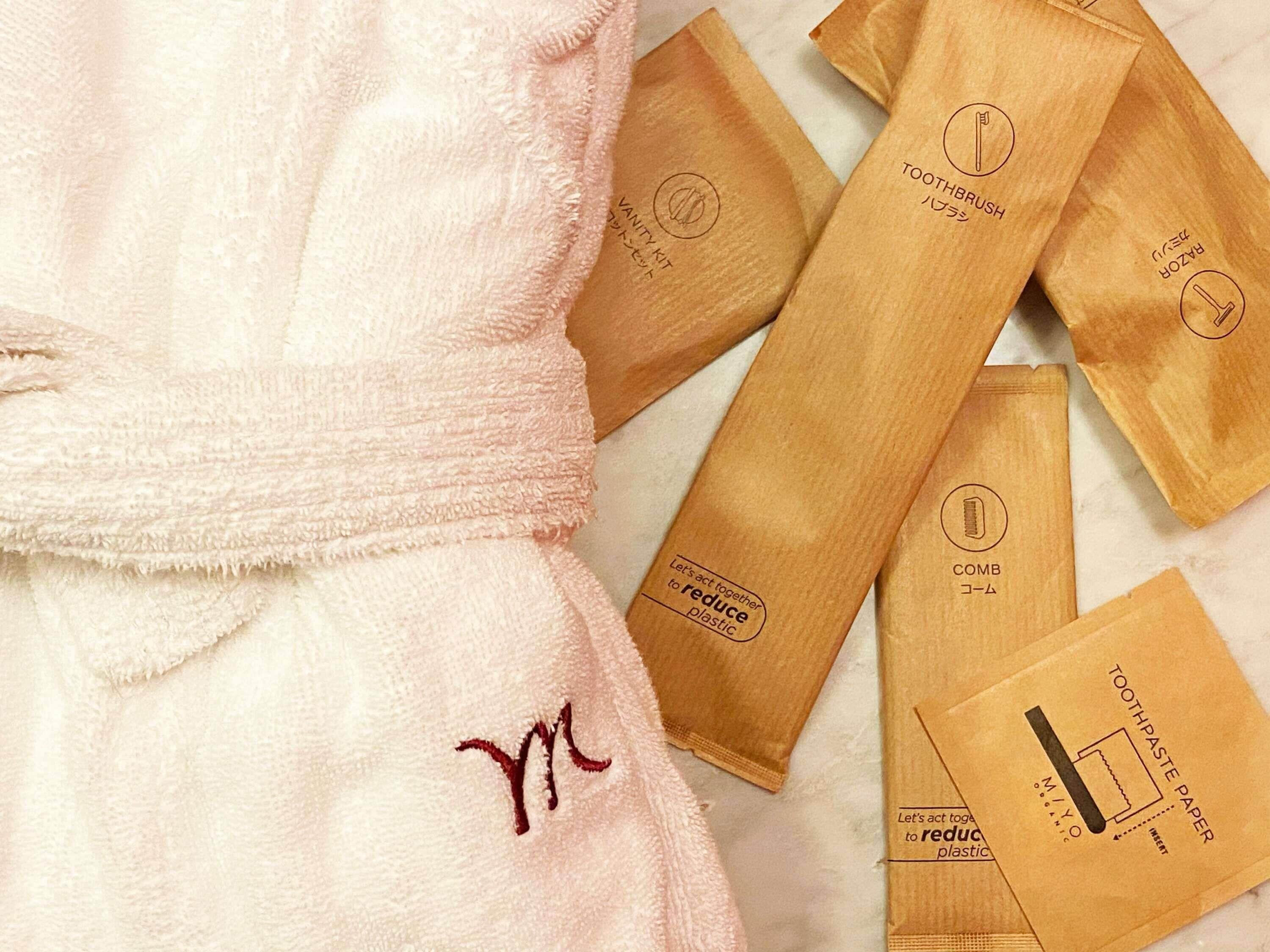 A pink robe with a monogram, and several brown paper bags with logos and text.