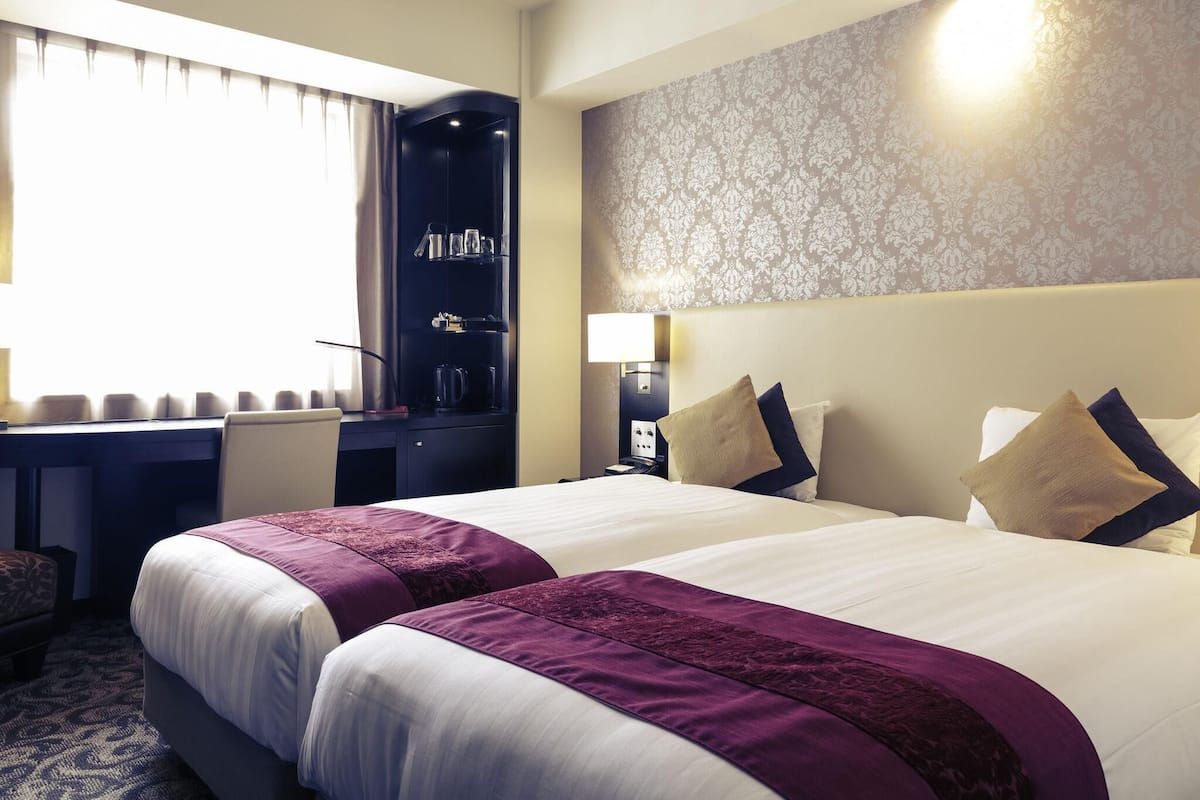 A hotel room with two beds, a desk, a wardrobe, and a nightstand.