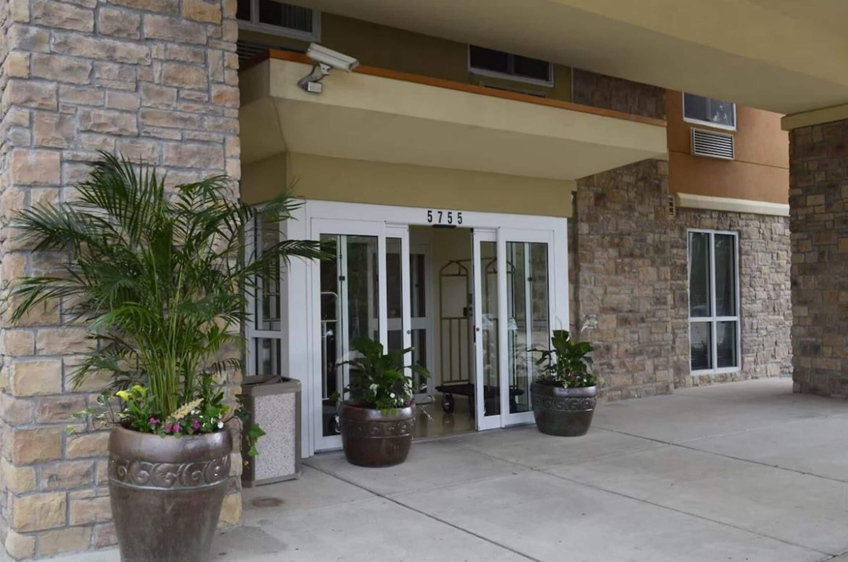 A building entrance with a stone facade, a number '5755' above the doors, and potted plants in front.