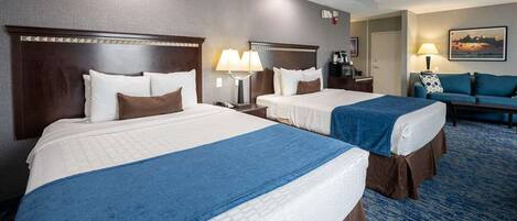 A hotel room with two beds, a sofa, and a desk.