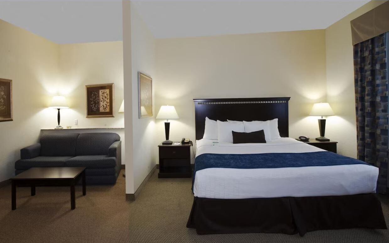 Quarto de hotel com uma cama grande, duas mesas de cabeceira com luminárias, um sofá e uma pequena mesa.