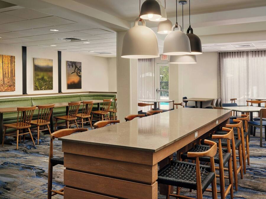 Un espace de restauration d'hôtel avec une longue table commune, plusieurs chaises et des luminaires suspendus.