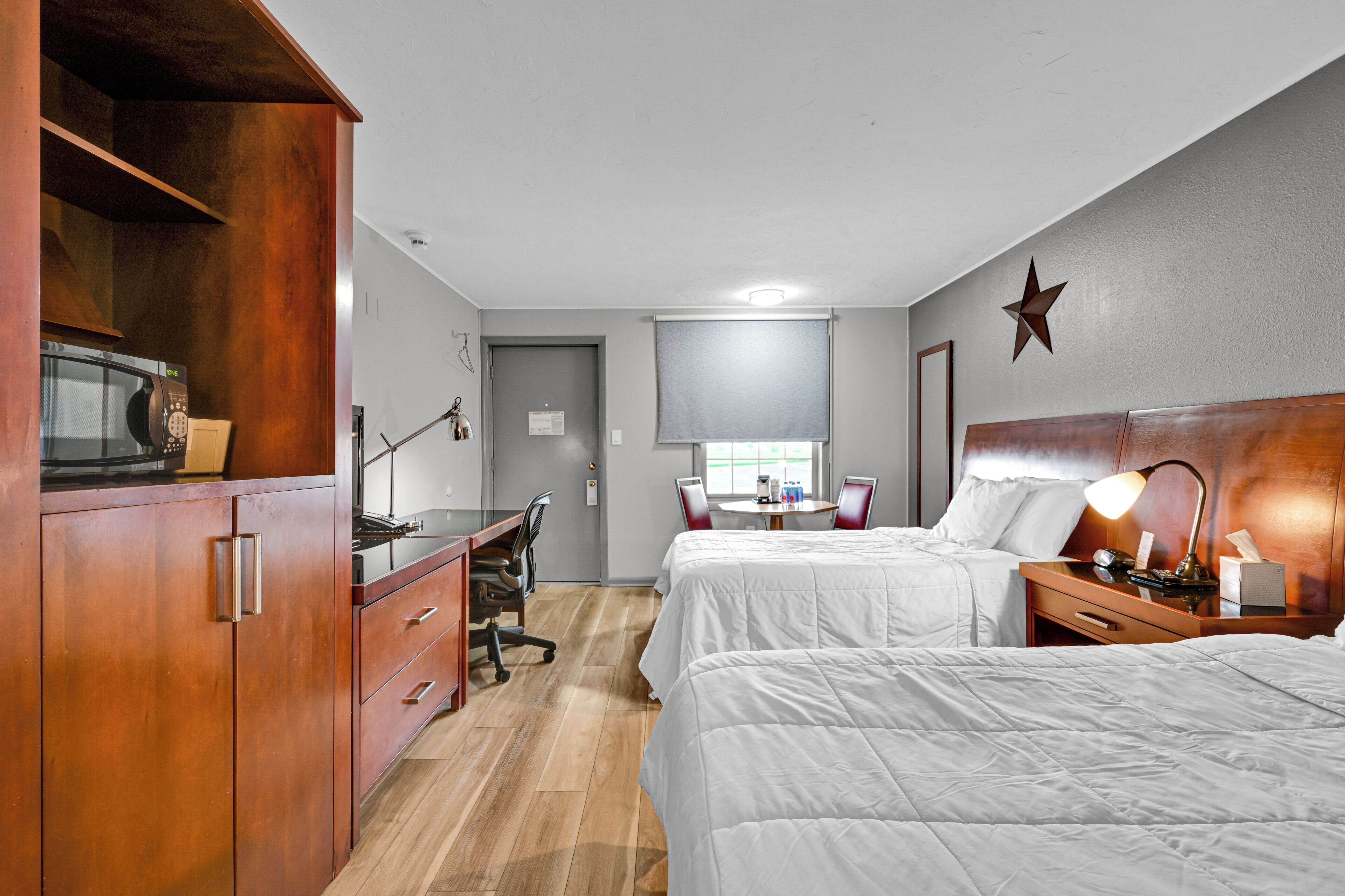 Een hotelkamer met twee bedden, een bureau met stoel, een magnetron, een lamp en een ster decoratie aan de muur.