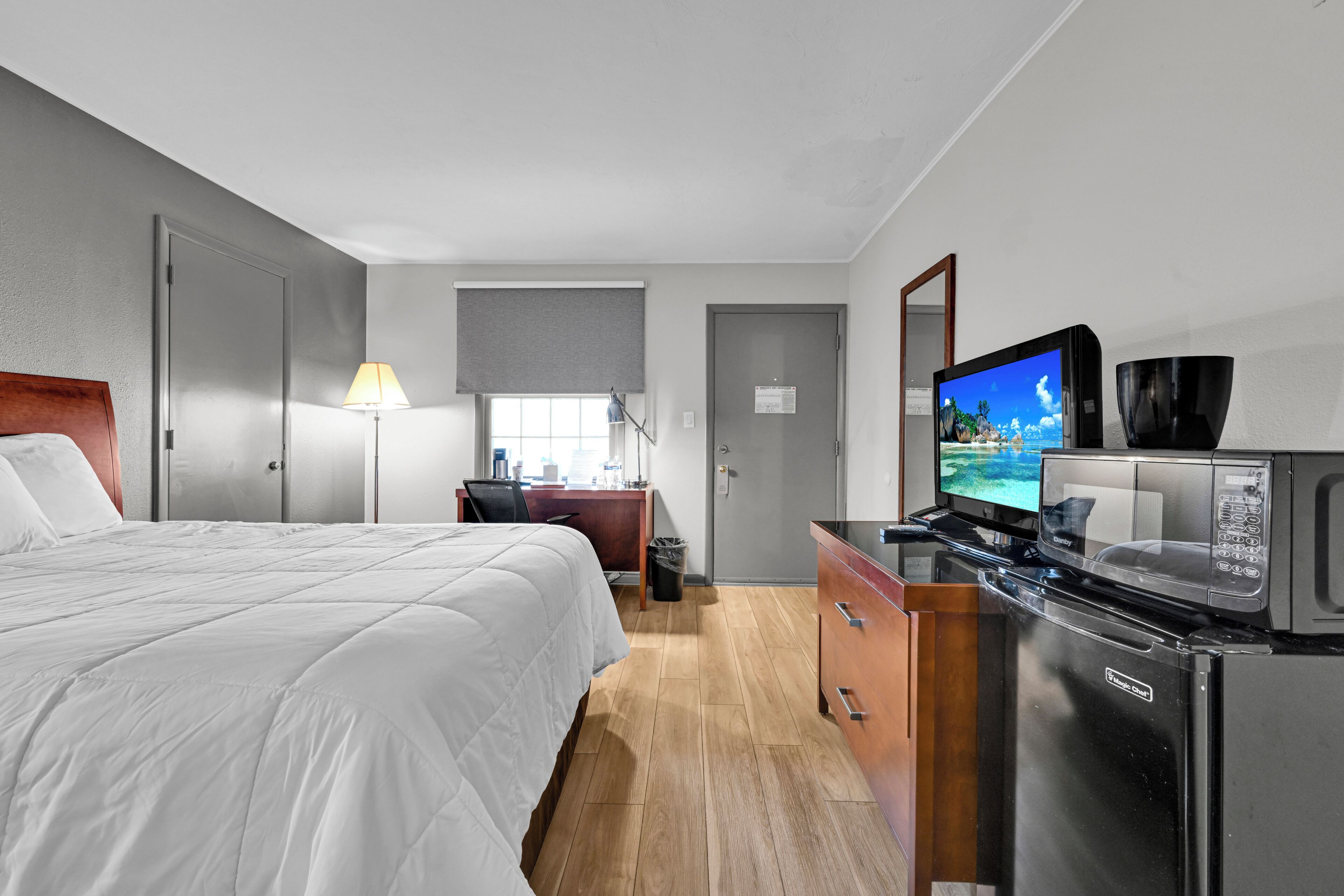 A hotel room with a bed, desk, television, microwave, and a dresser.