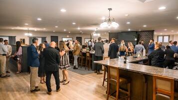 A spacious indoor area with a bar, wooden flooring, and modern lighting fixtures.