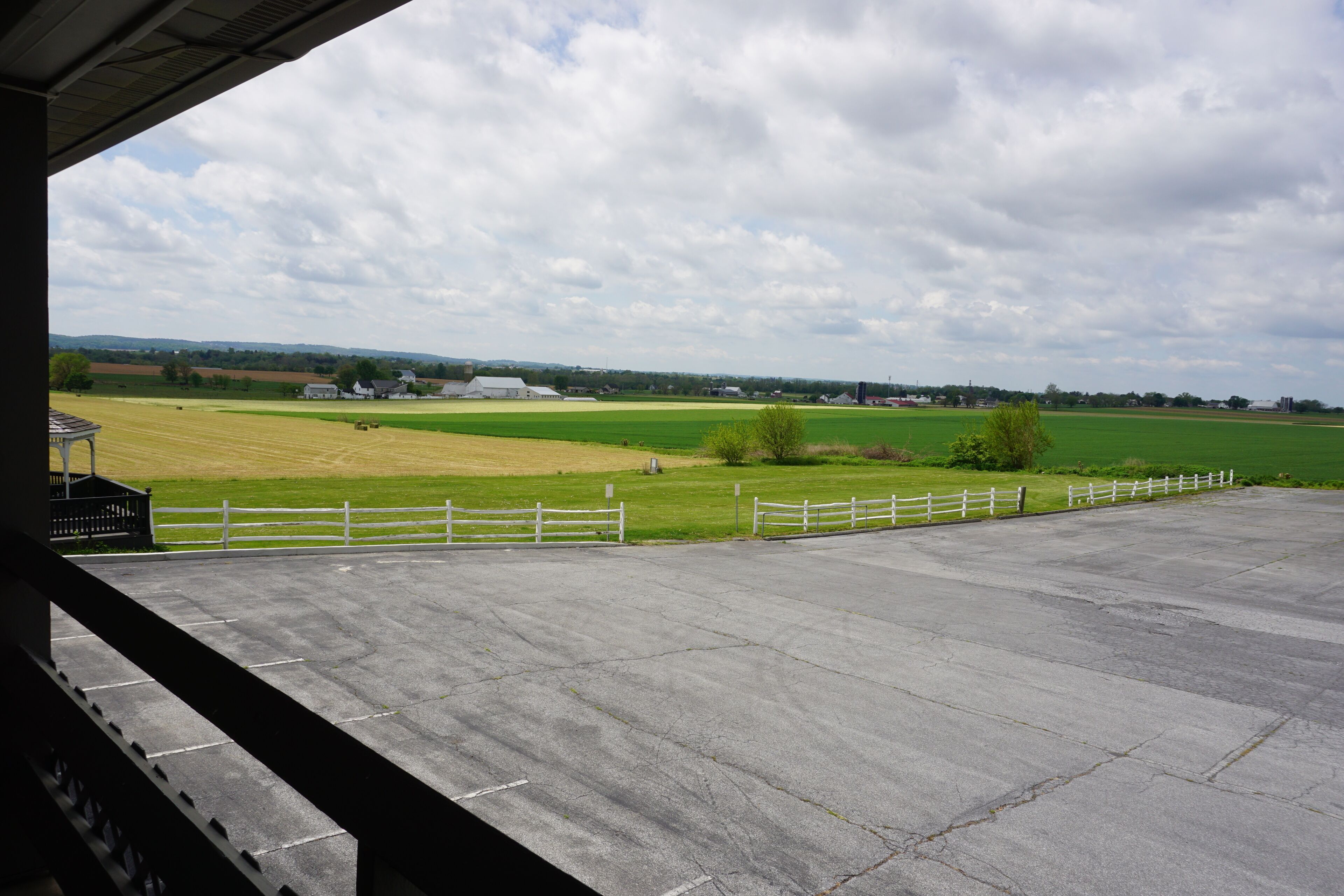A concrete viewing platform with a white fence, overlooking a green field and distant buildings.