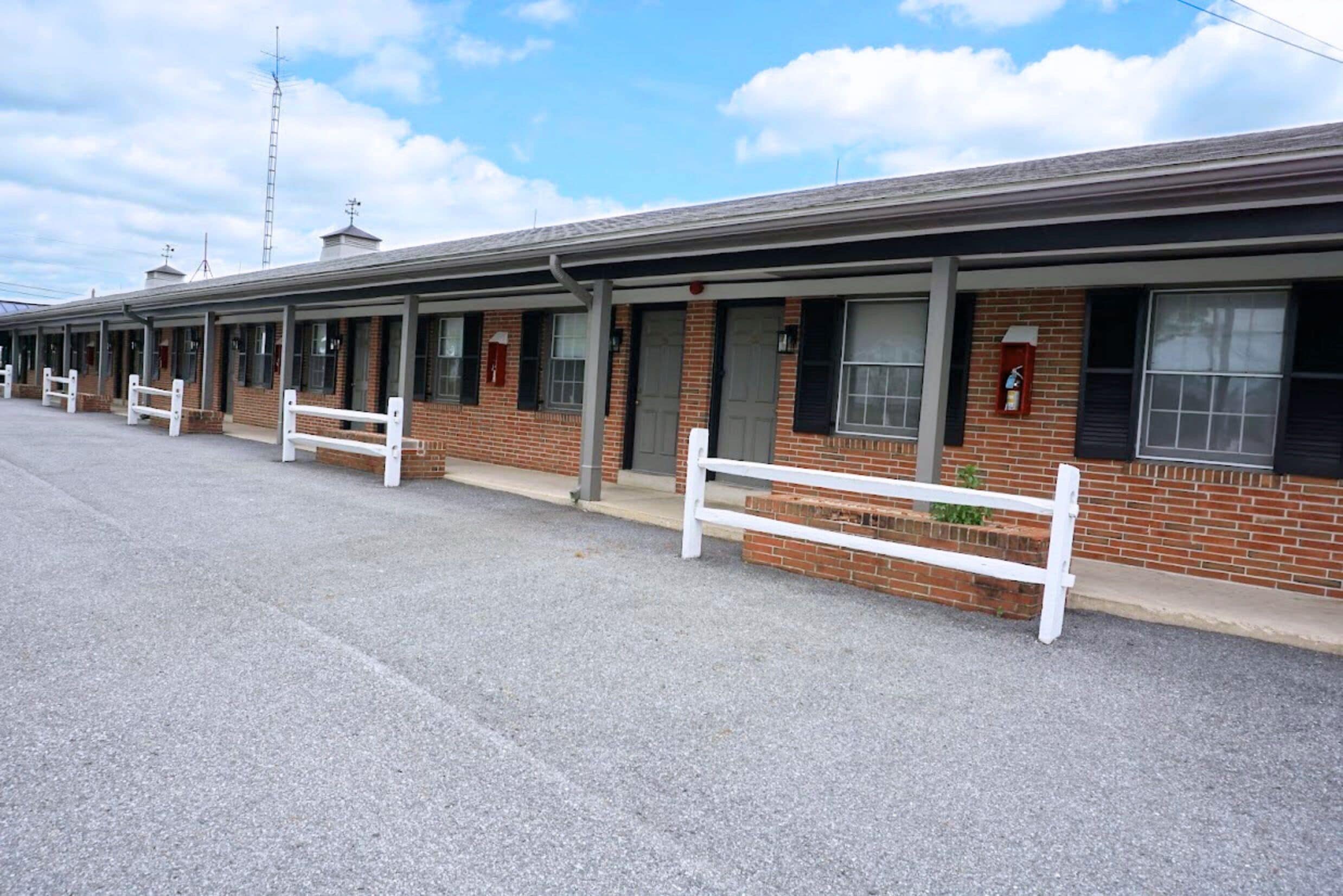 Hileras de habitaciones de motel con puertas individuales, un corredor cubierto y un estacionamiento.