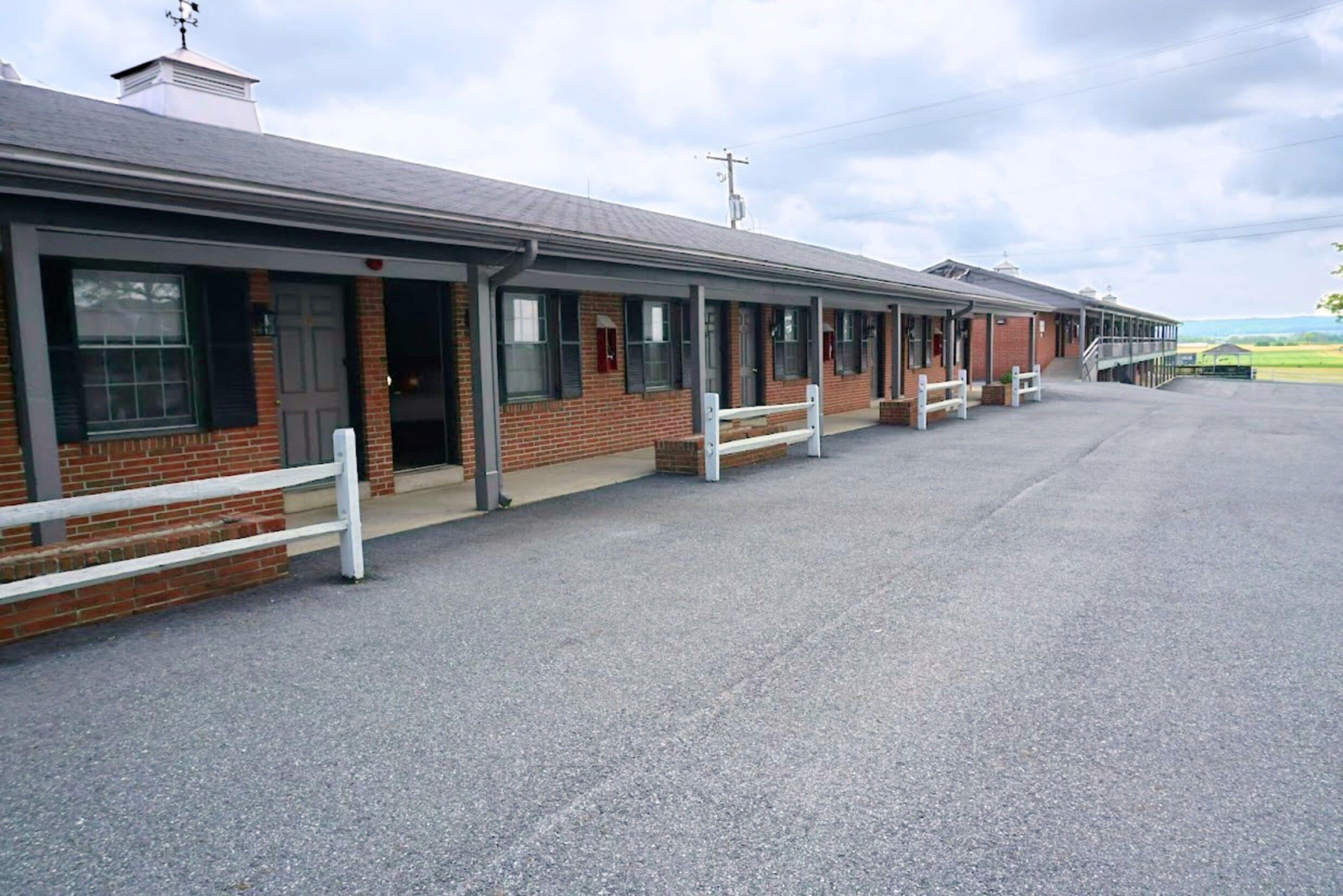 A row of single-story buildings with a flat roof, likely a motel or inn, with a paved driveway and no visible landscaping.