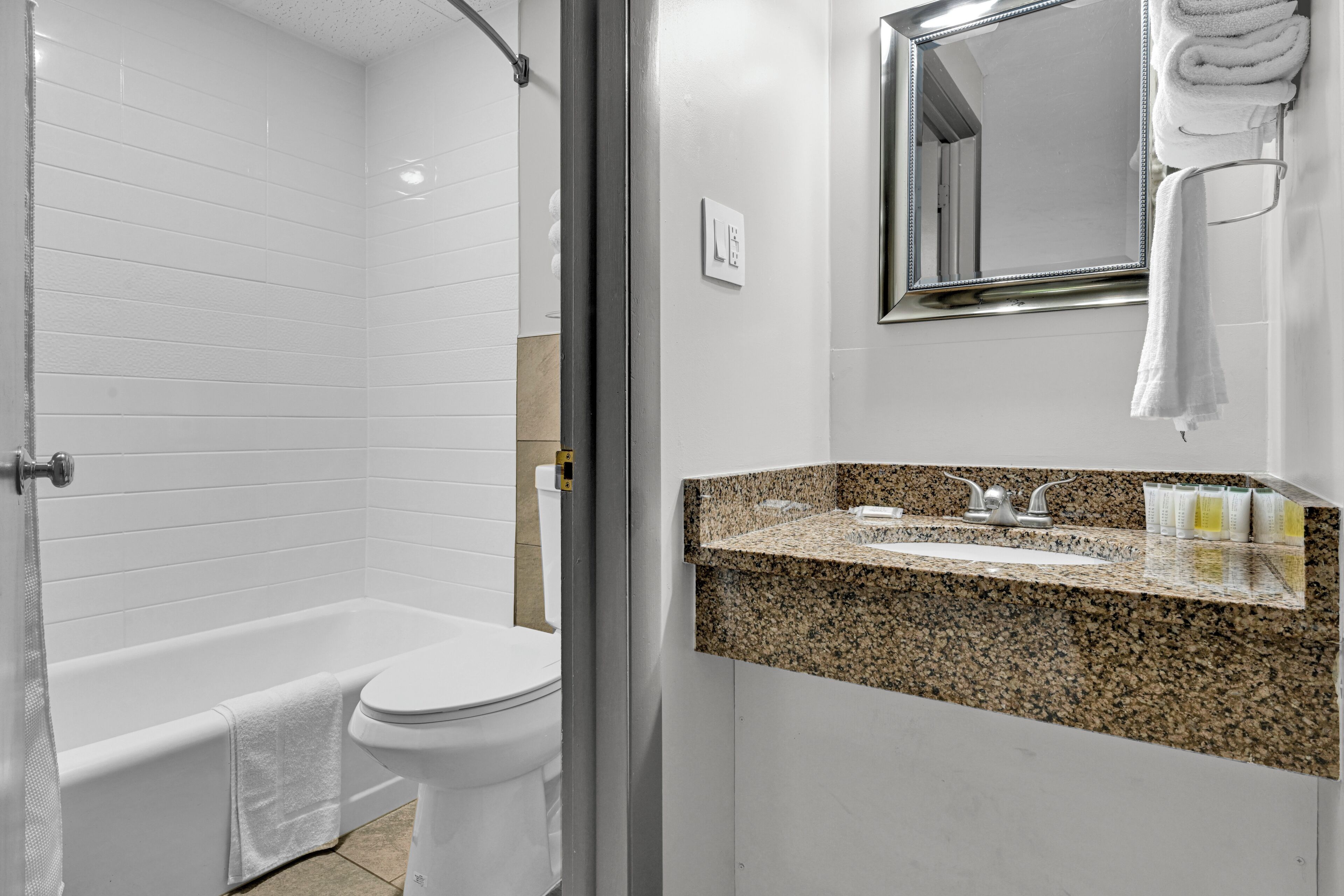 A bathroom with a white bathtub, a toilet, a granite countertop sink, and a mirror above the sink.