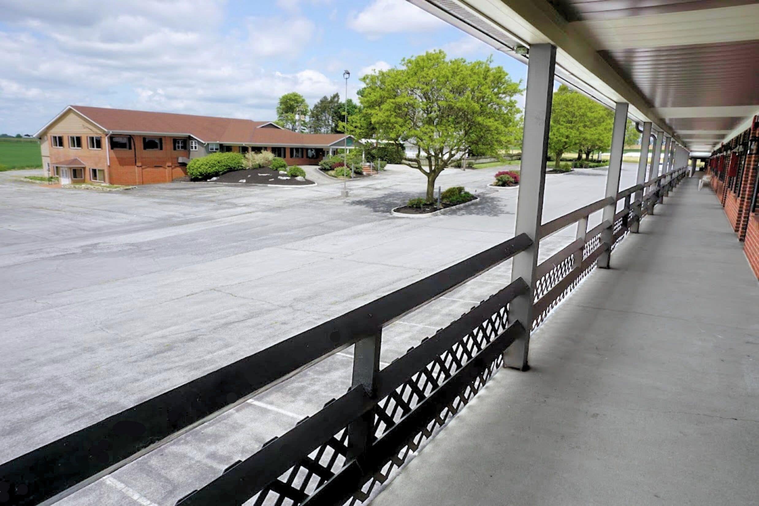 A covered outdoor area with a concrete floor, a metal railing, and a building in the background.