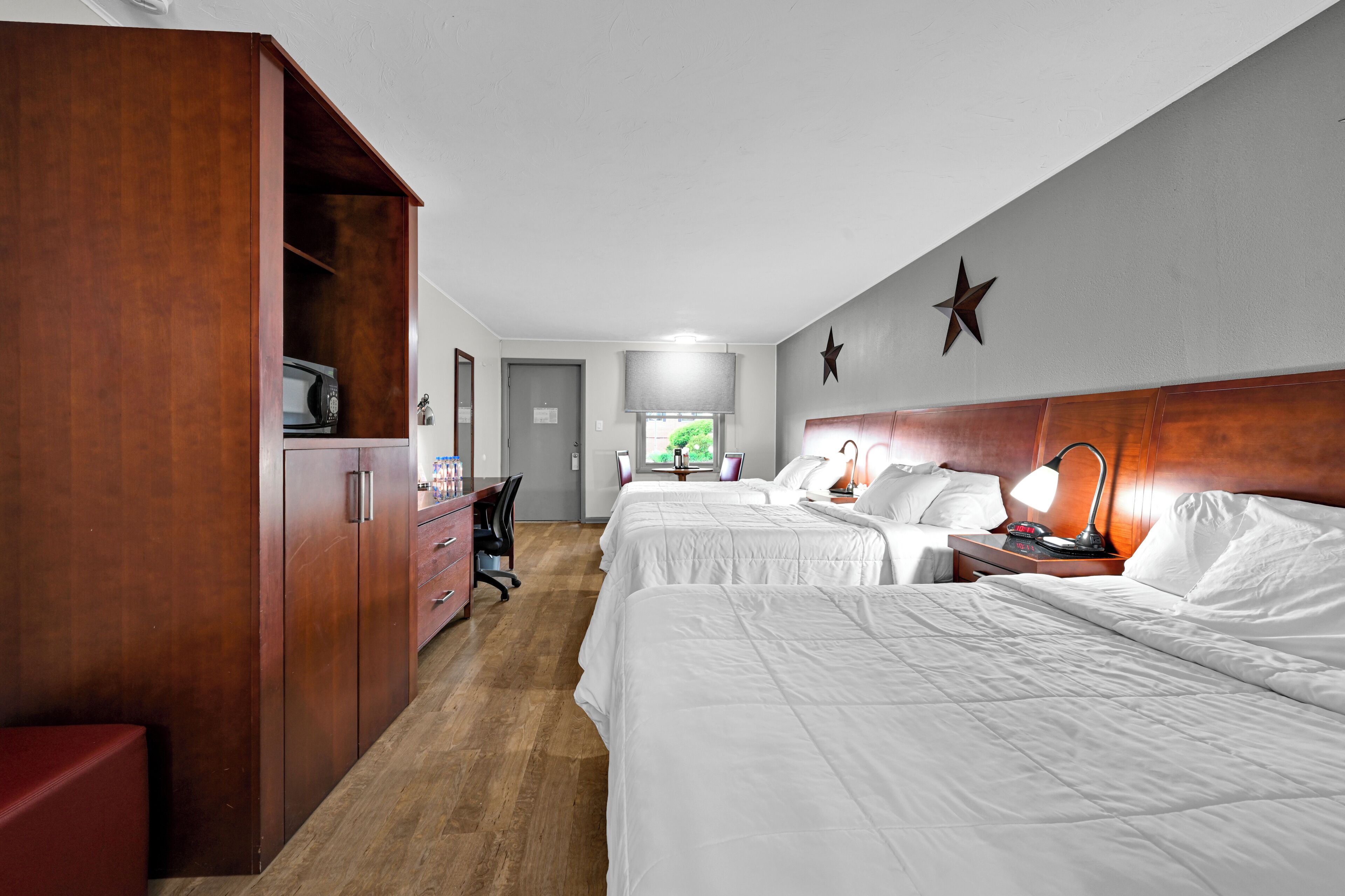 A hotel room with two beds, a desk, a wardrobe, and a view of the outdoors.