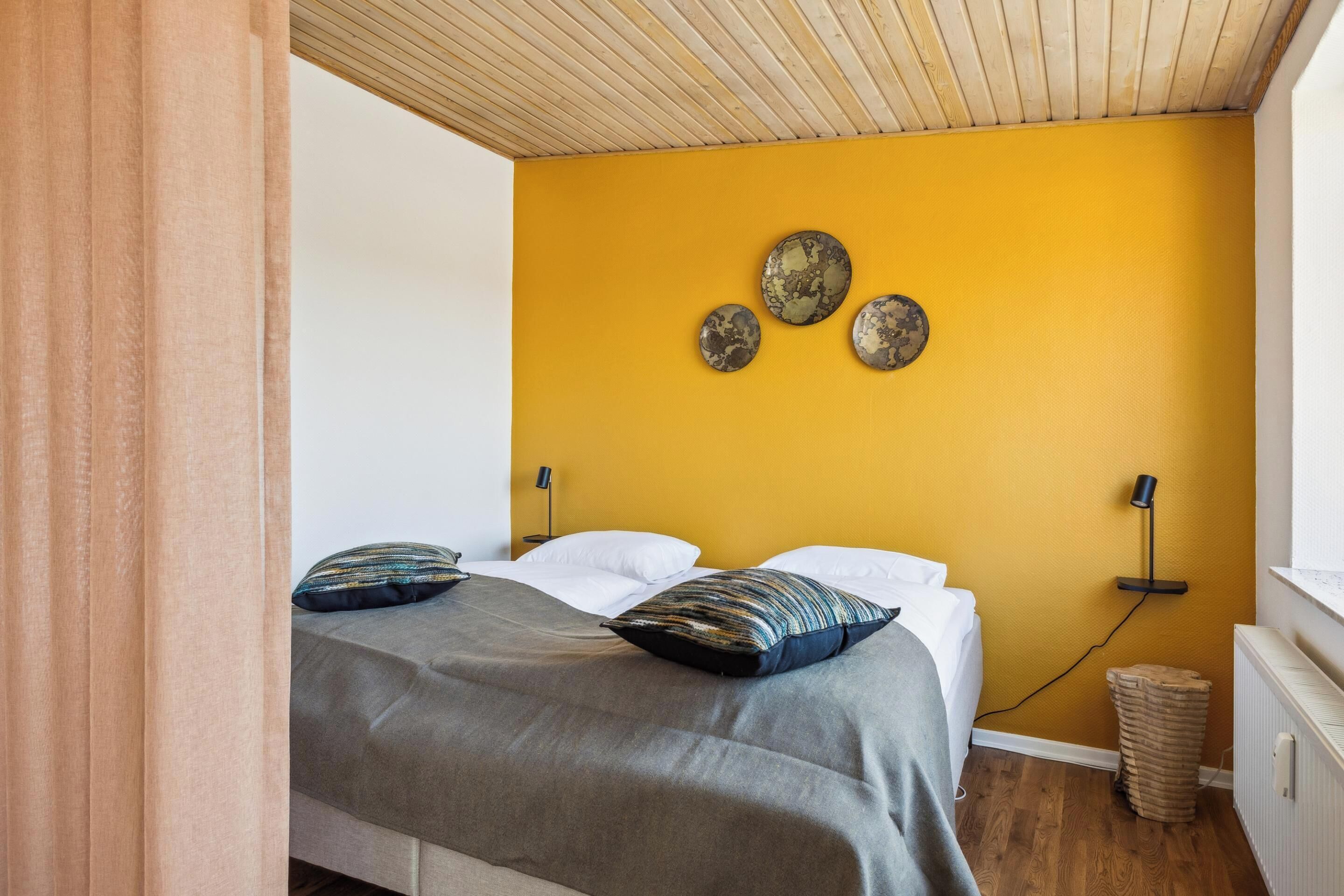 Een slaapkamer met een bed, een gele wand en een houten plafond.