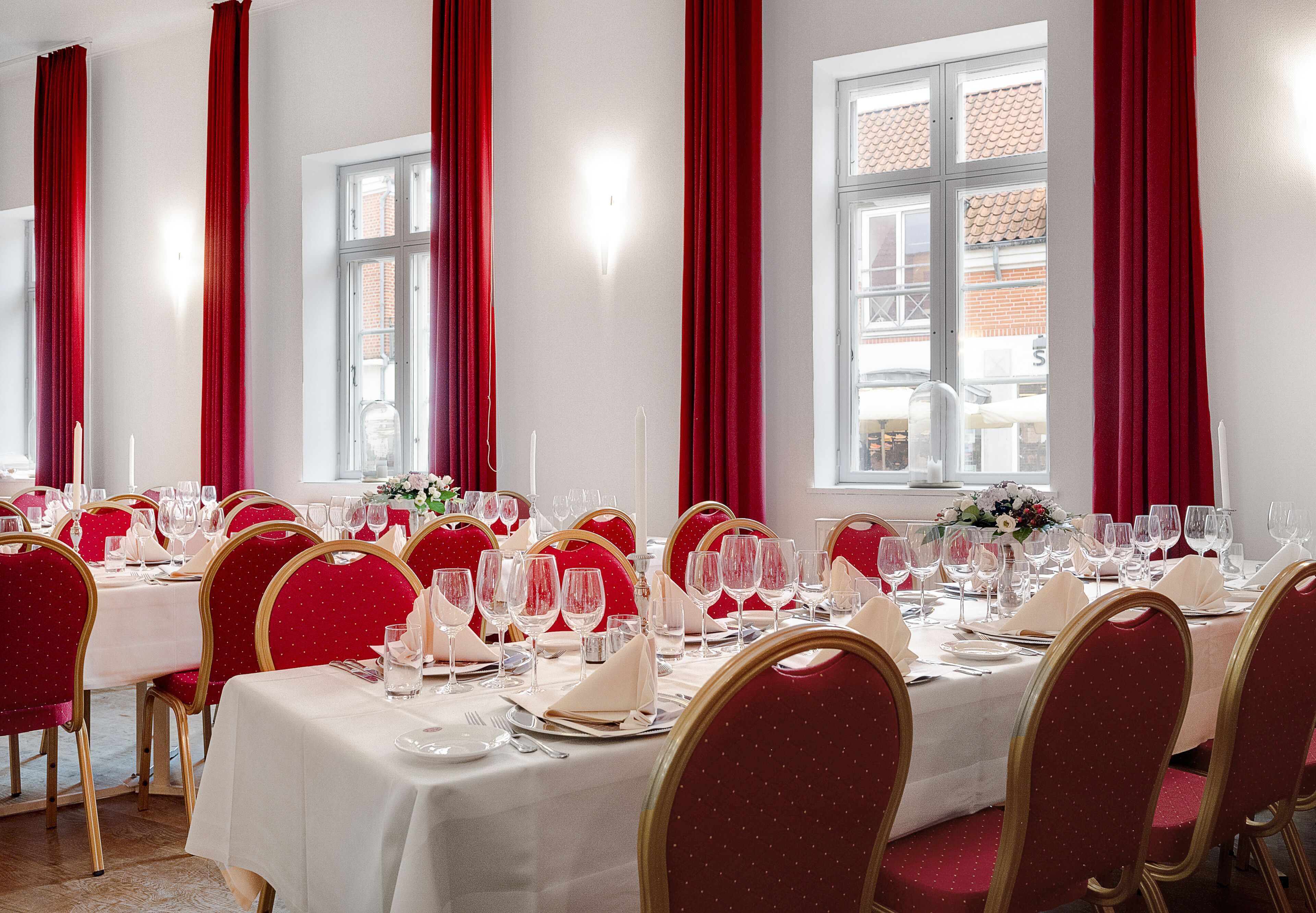 A dining area with tables set for a meal, red curtains, and large windows.