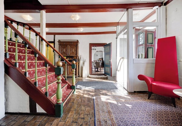 A staircase with wooden balusters and a red carpet leading to a room with a red chair and a view of the kitchen through an open door. - Hotel Ringkjøbing (Ringkobing)