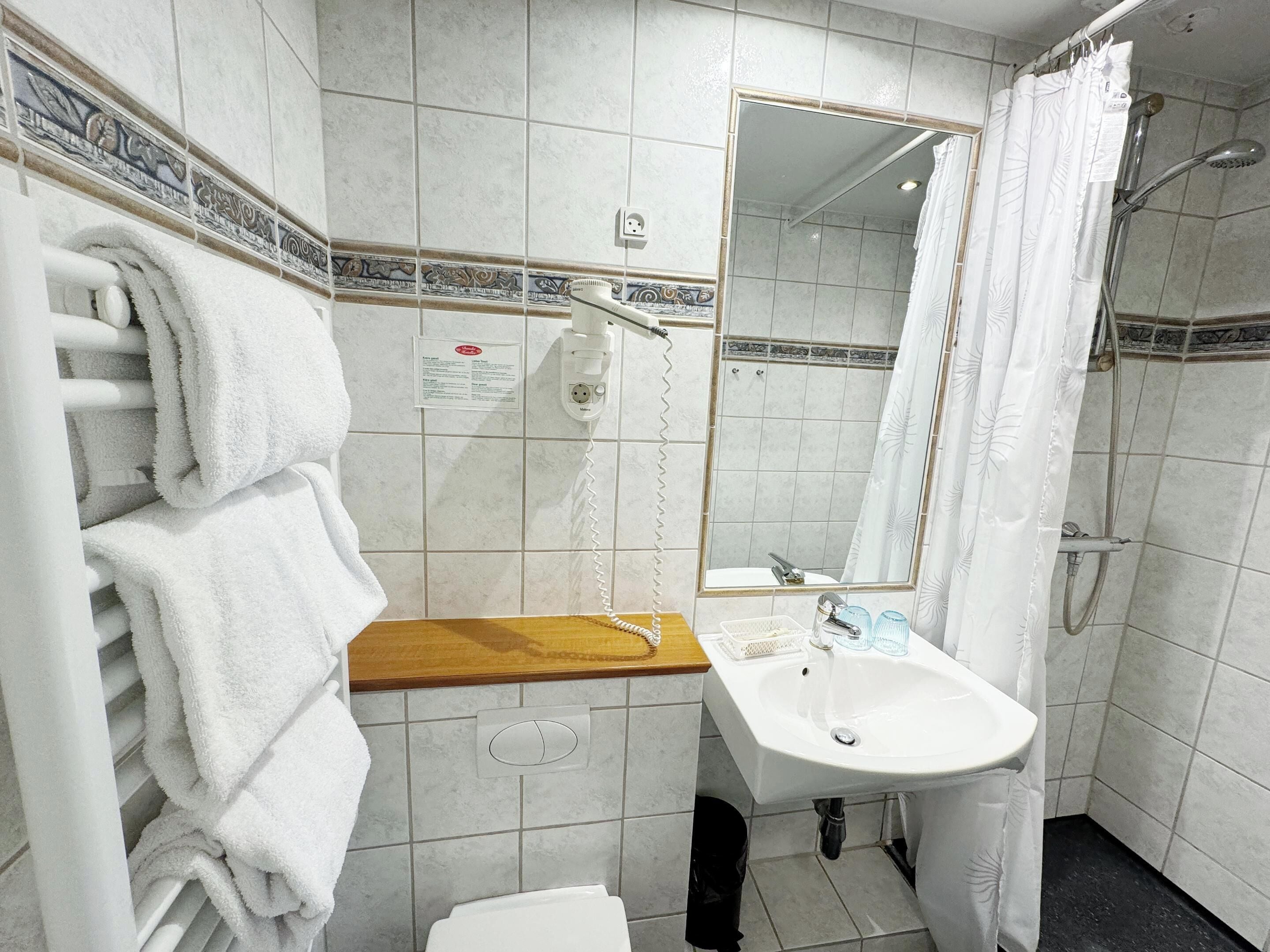 Ein Badezimmer mit weißem Waschbecken, einem Spiegel, einer Duschkabine und einem Handtuchhalter mit Handtüchern.