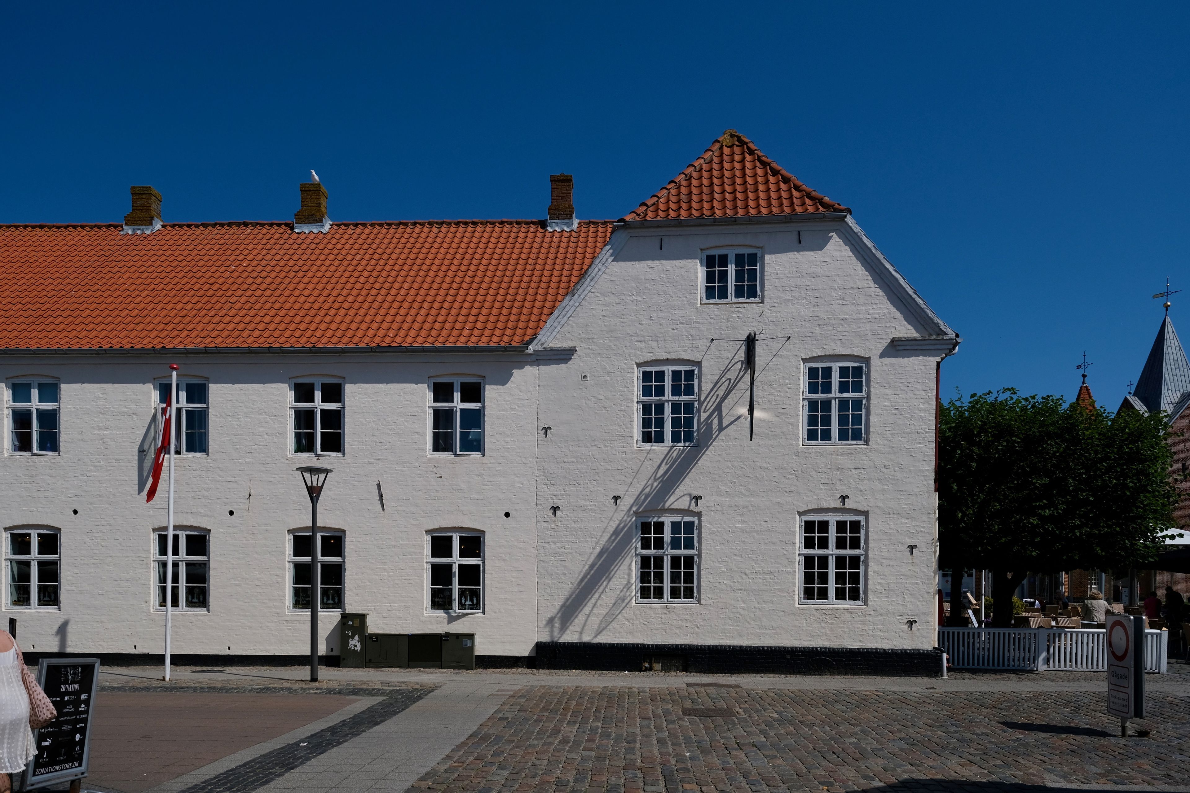 A white building with a red-tiled roof, multiple windows, and a staircase leading to the upper floor.