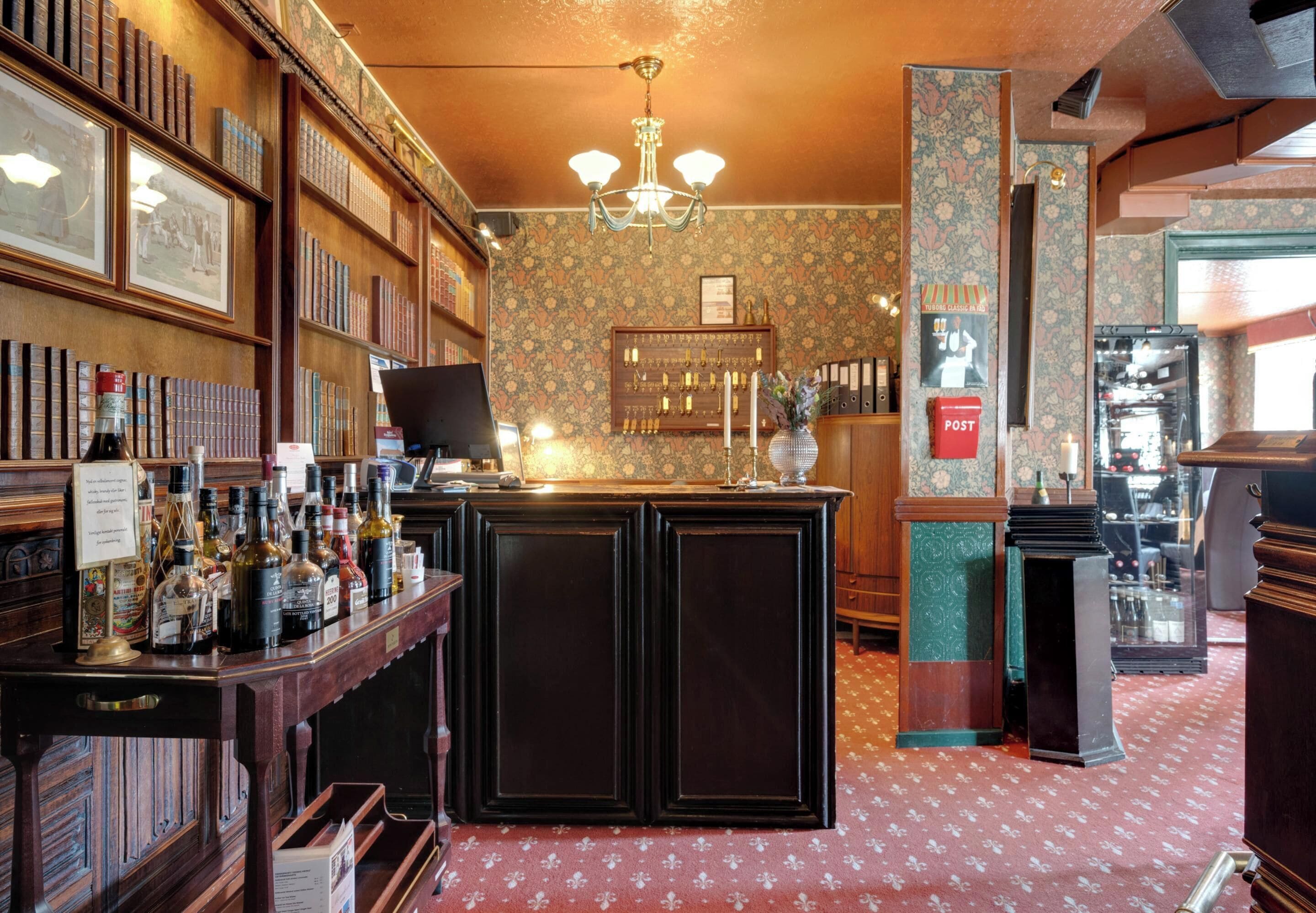 A bar area with a wooden counter, shelves with bottles, and framed pictures on the wall.