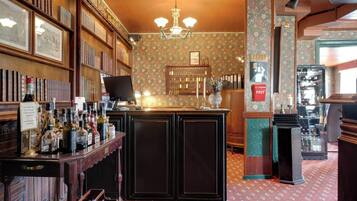 A bar area with a wooden counter, shelves with bottles, and framed pictures on the wall.