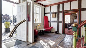A traditional interior with exposed wooden beams, a red chair, and a view through a door to the outside. - Hotel Ringkjøbing (Ringkobing)