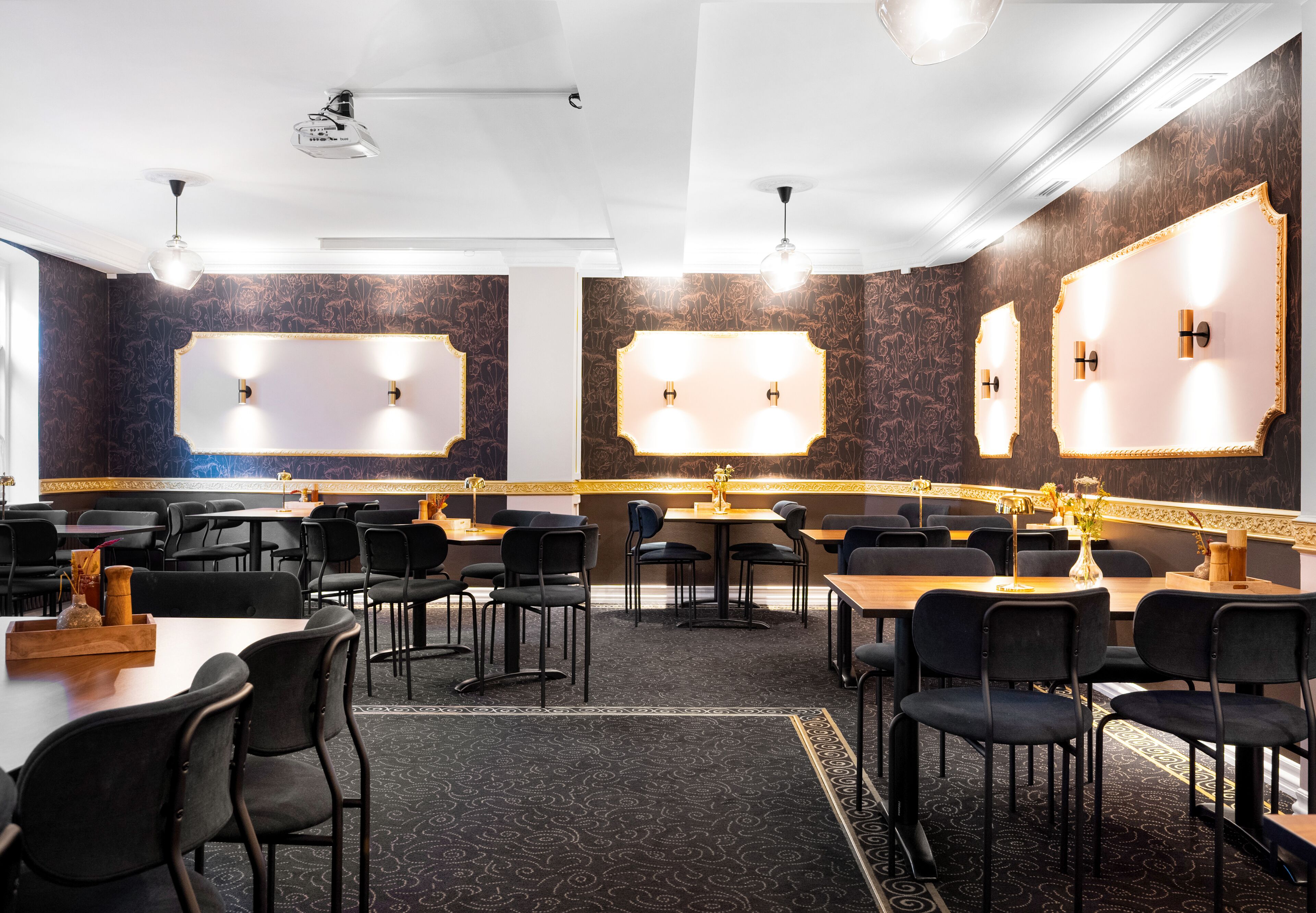 A conference room with tables and chairs, a projector, and wall-mounted lighting.