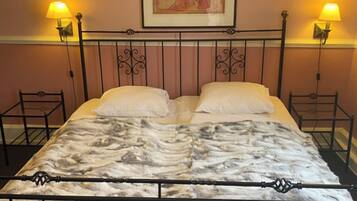 A bed with a metal frame and a patterned bedspread, flanked by two bedside lamps and a framed picture on the wall.
