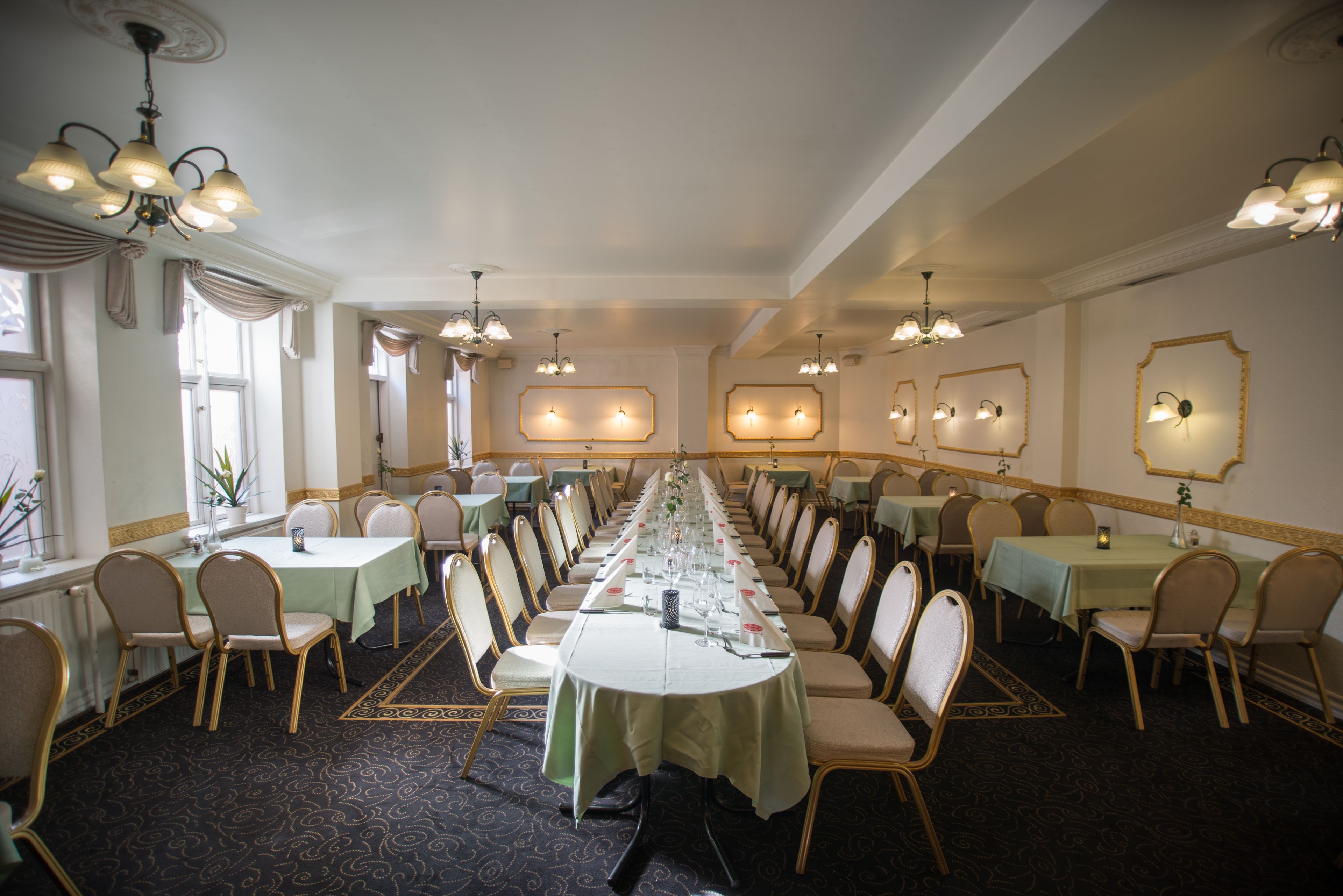 Un salón de banquetes con mesas largas, sillas, candelabros y apliques de pared.