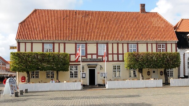 A traditional half-timbered building with a red-tiled roof, a sign reading "Hotel Kingjobing," and two flagpoles. - Hotel Ringkjøbing (Ringkobing)