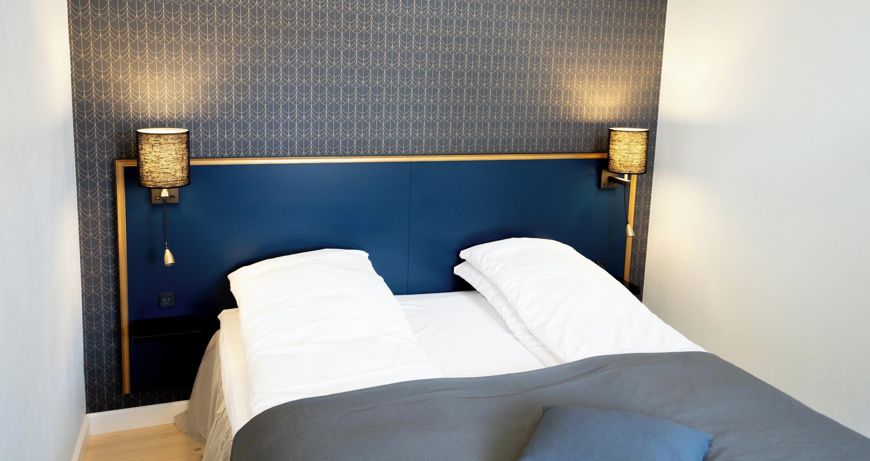 A hotel room with a blue headboard, two bedside lamps, and a bed with white linens.