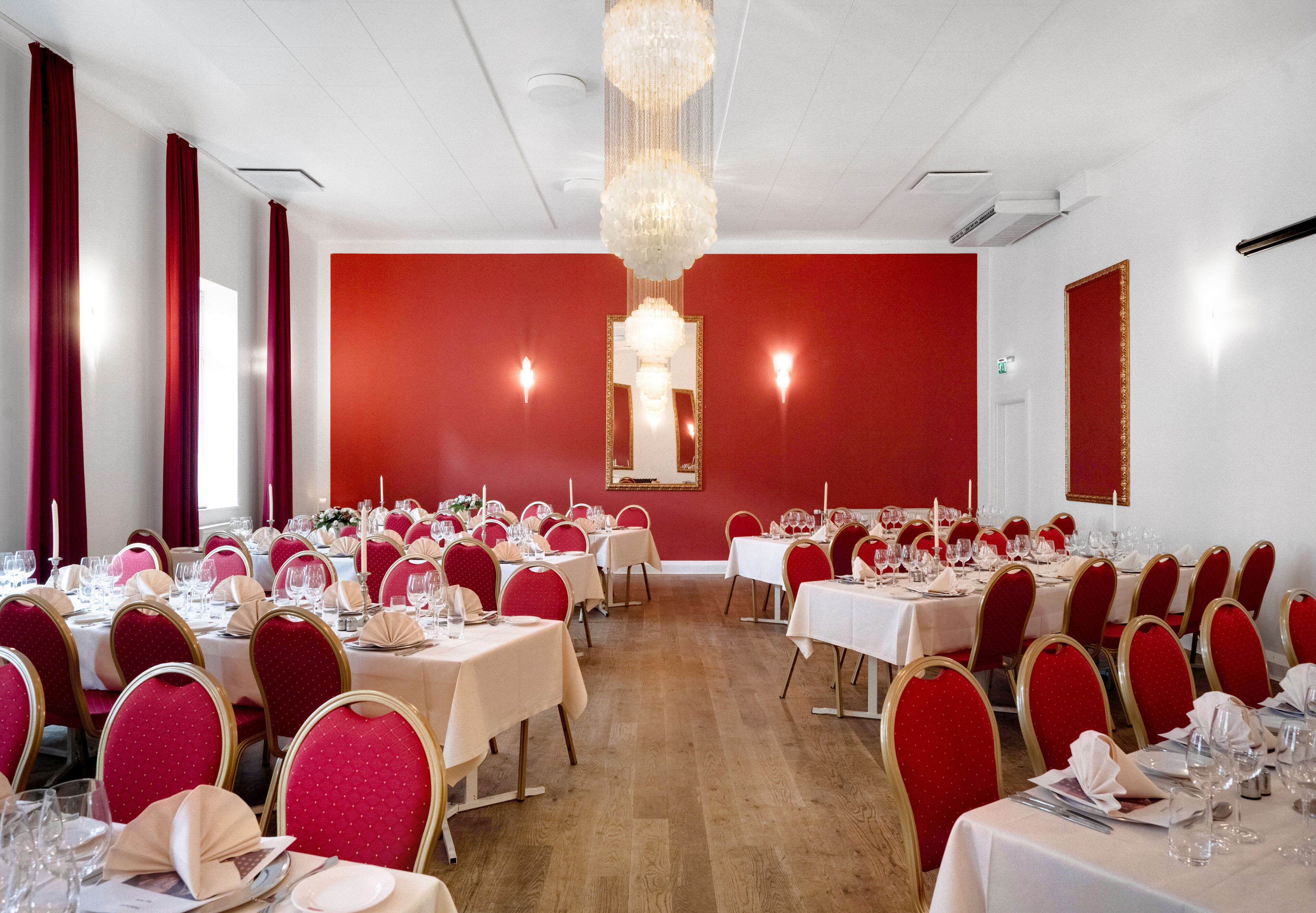 Een balzaal met gedekte tafels voor een formeel evenement, rode stoelen en een kroonluchter.