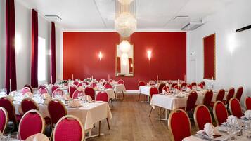 Un salón de banquetes con mesas dispuestas para un evento formal, sillas rojas y una araña.