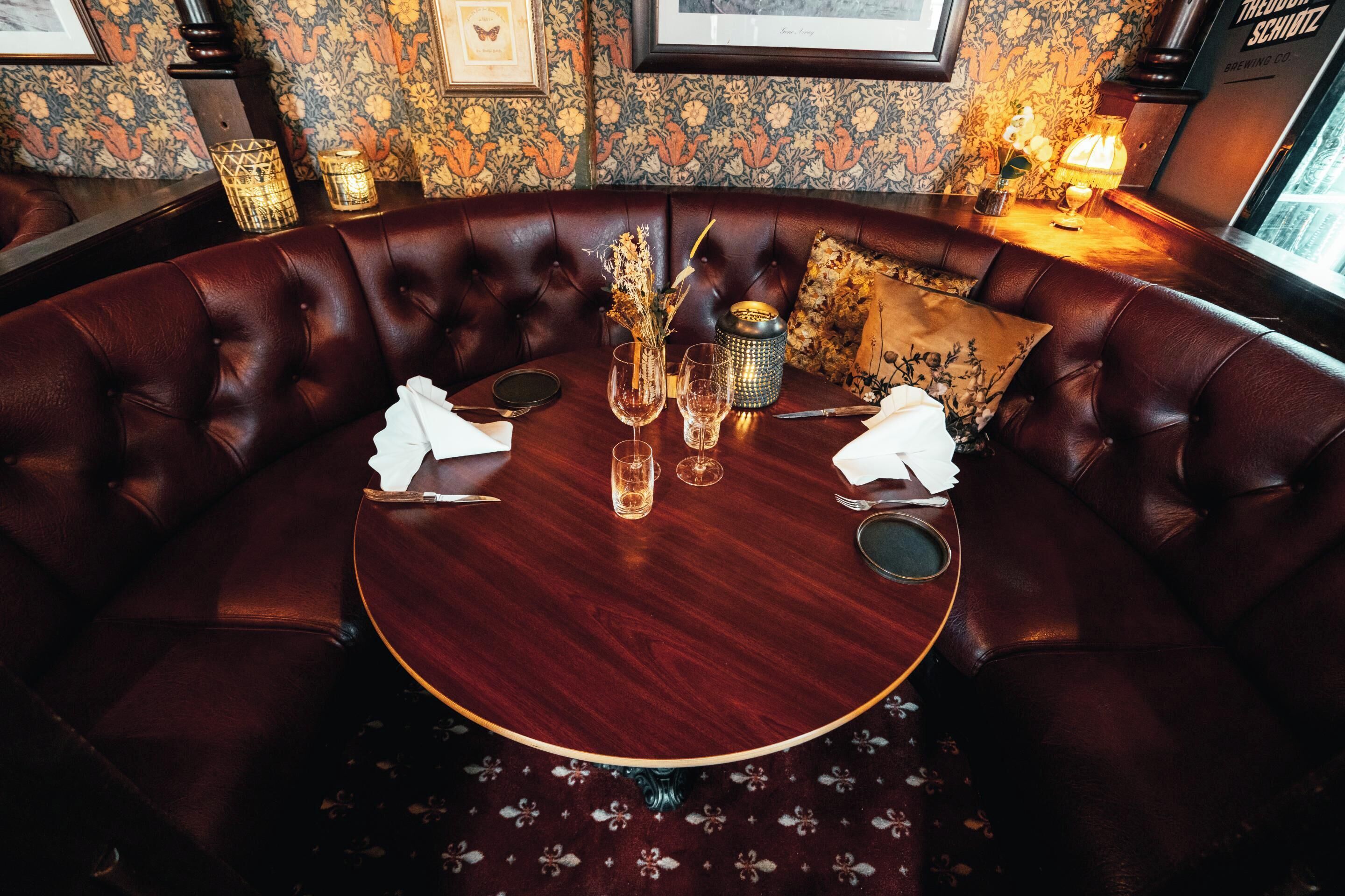 A round table with a dark wood finish, surrounded by a leather sofa with a tufted design.