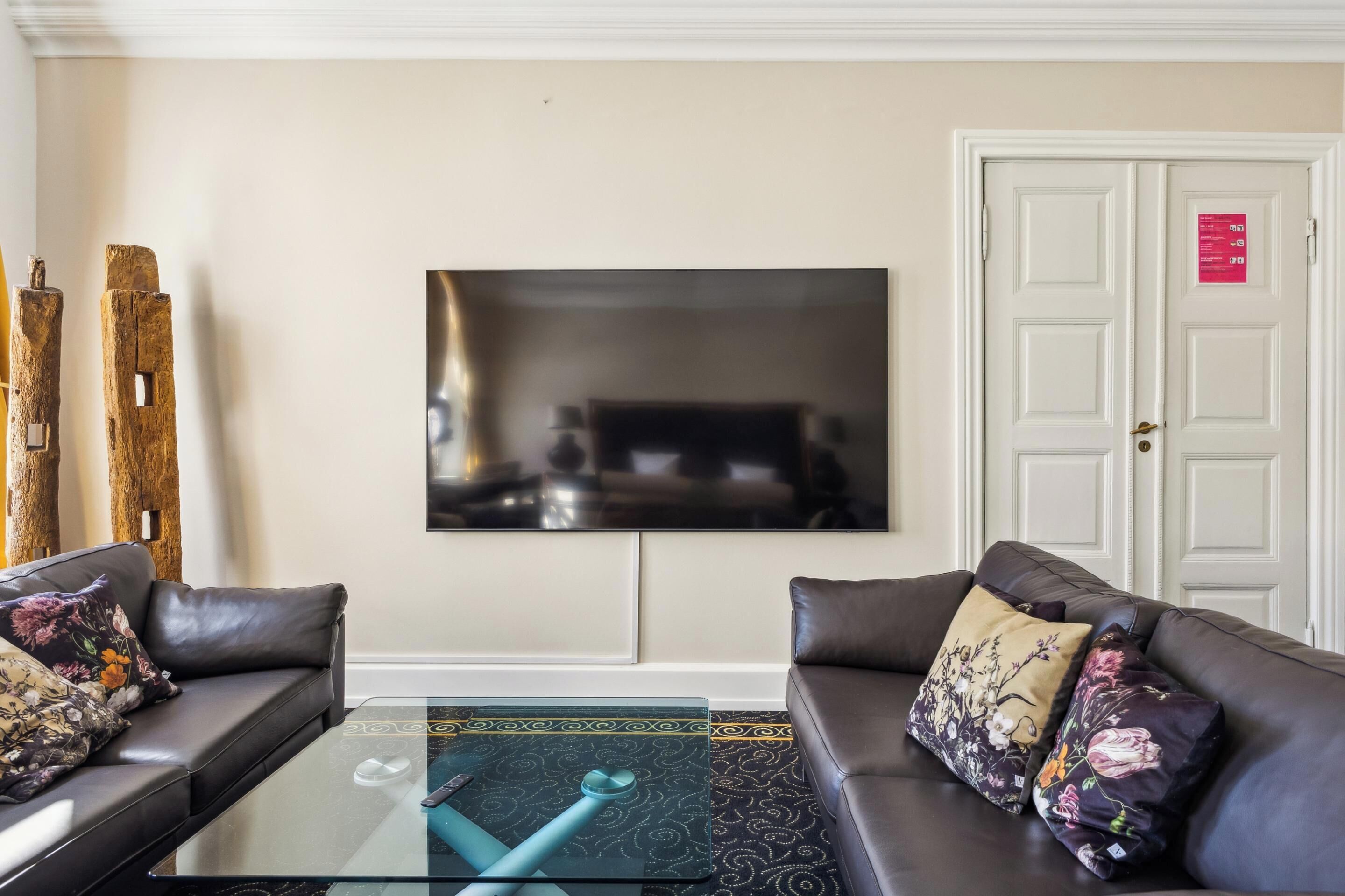 A modern living room with two leather sofas, a glass coffee table, and a flat-screen TV mounted on the wall.
