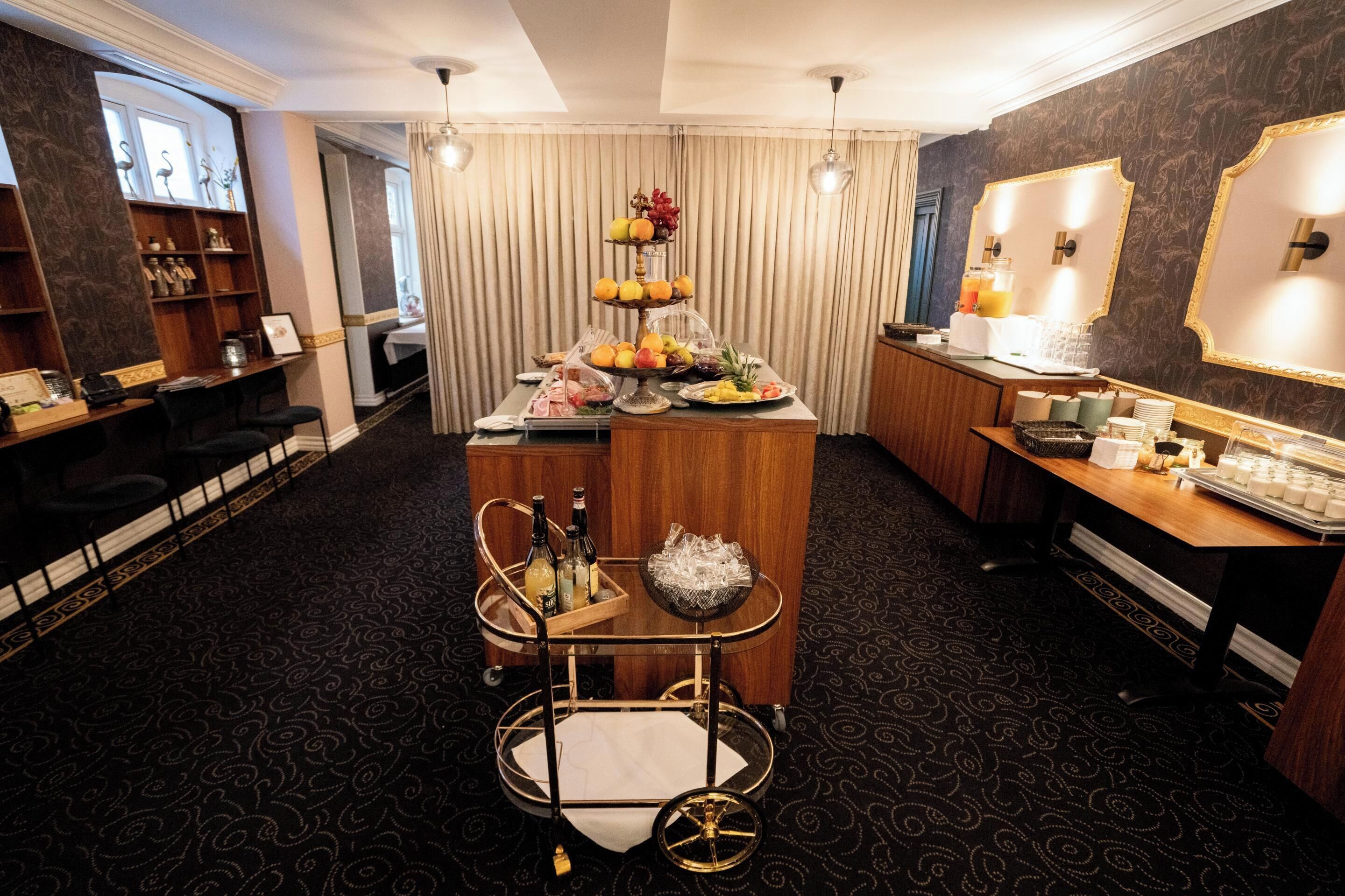 A hotel room with a bar area, a desk with a computer, and a dining table with a fruit display.