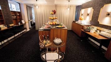 Une chambre d’hôtel comprenant un coin bar, un bureau avec un ordinateur et une table à manger agrémentée d’un présentoir de fruits.