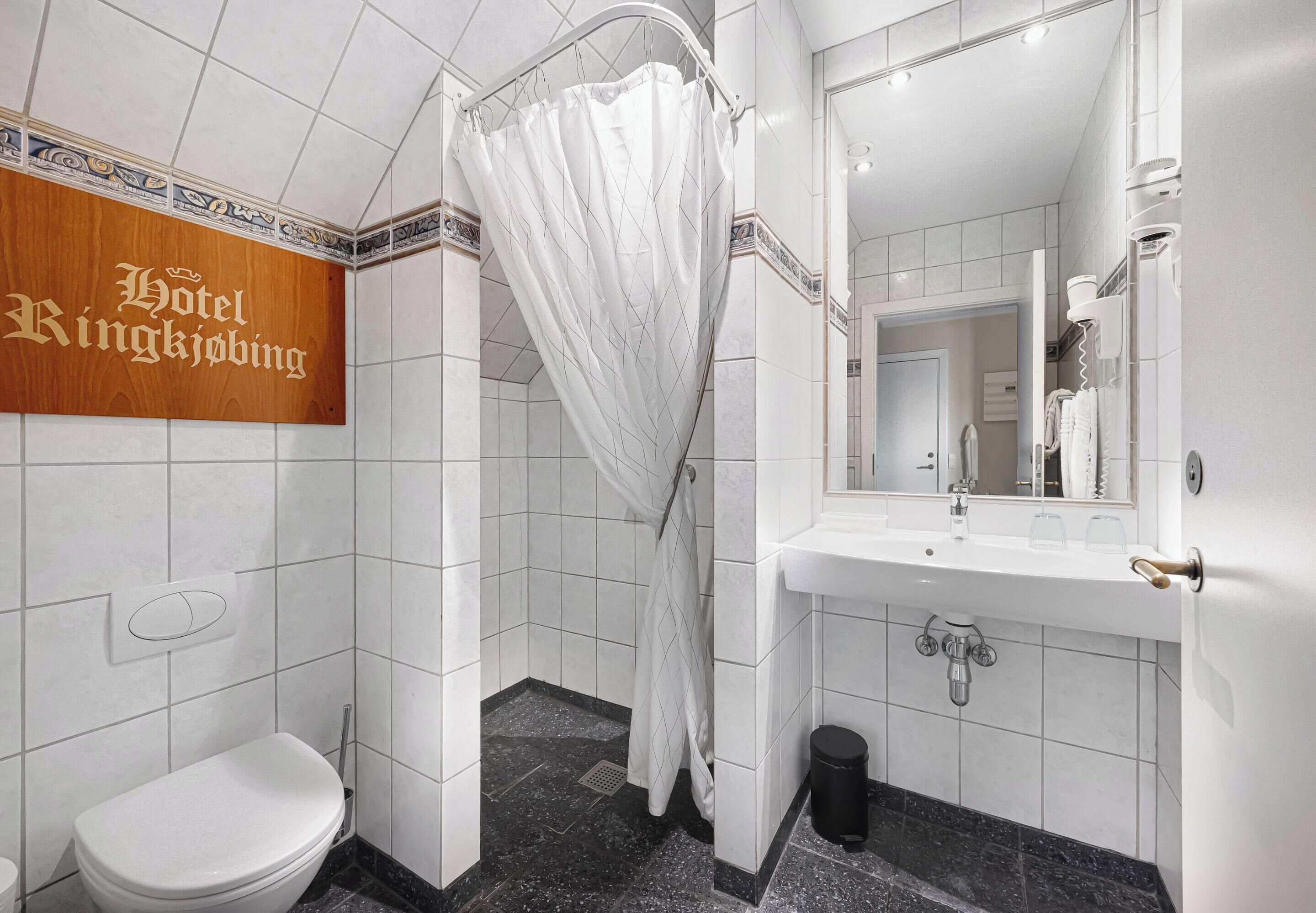 A hotel bathroom with a shower, toilet, sink, and a mirror.