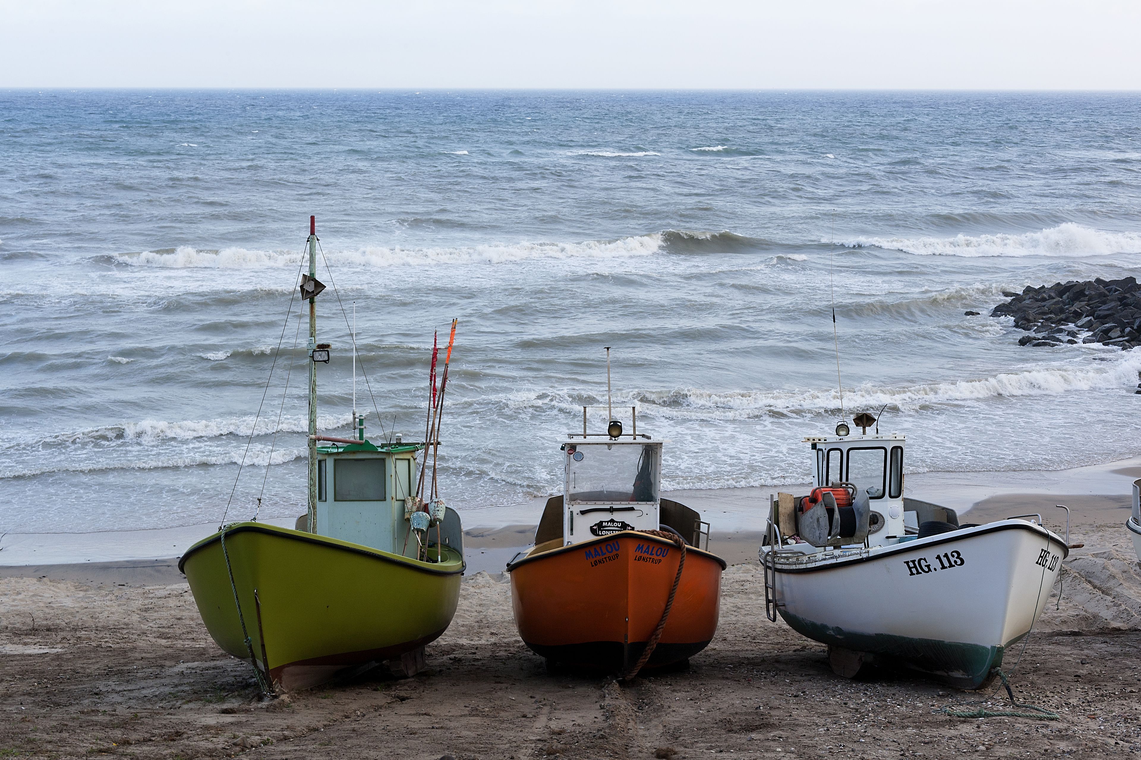 Three boats on a sandy beach near the water.