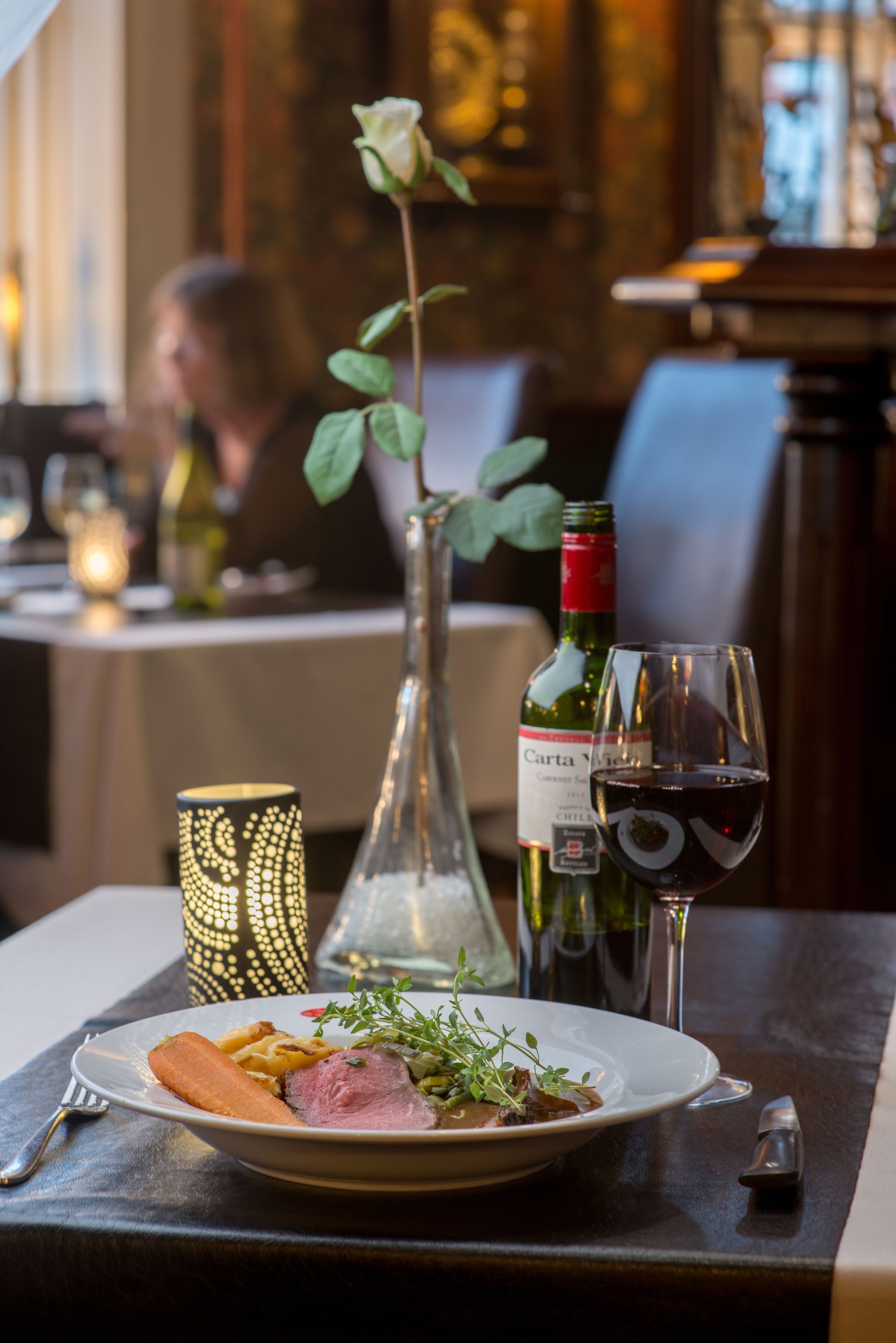 Una mesa de comedor con un plato de comida, una botella de vino, una copa de vino y un candelabro.